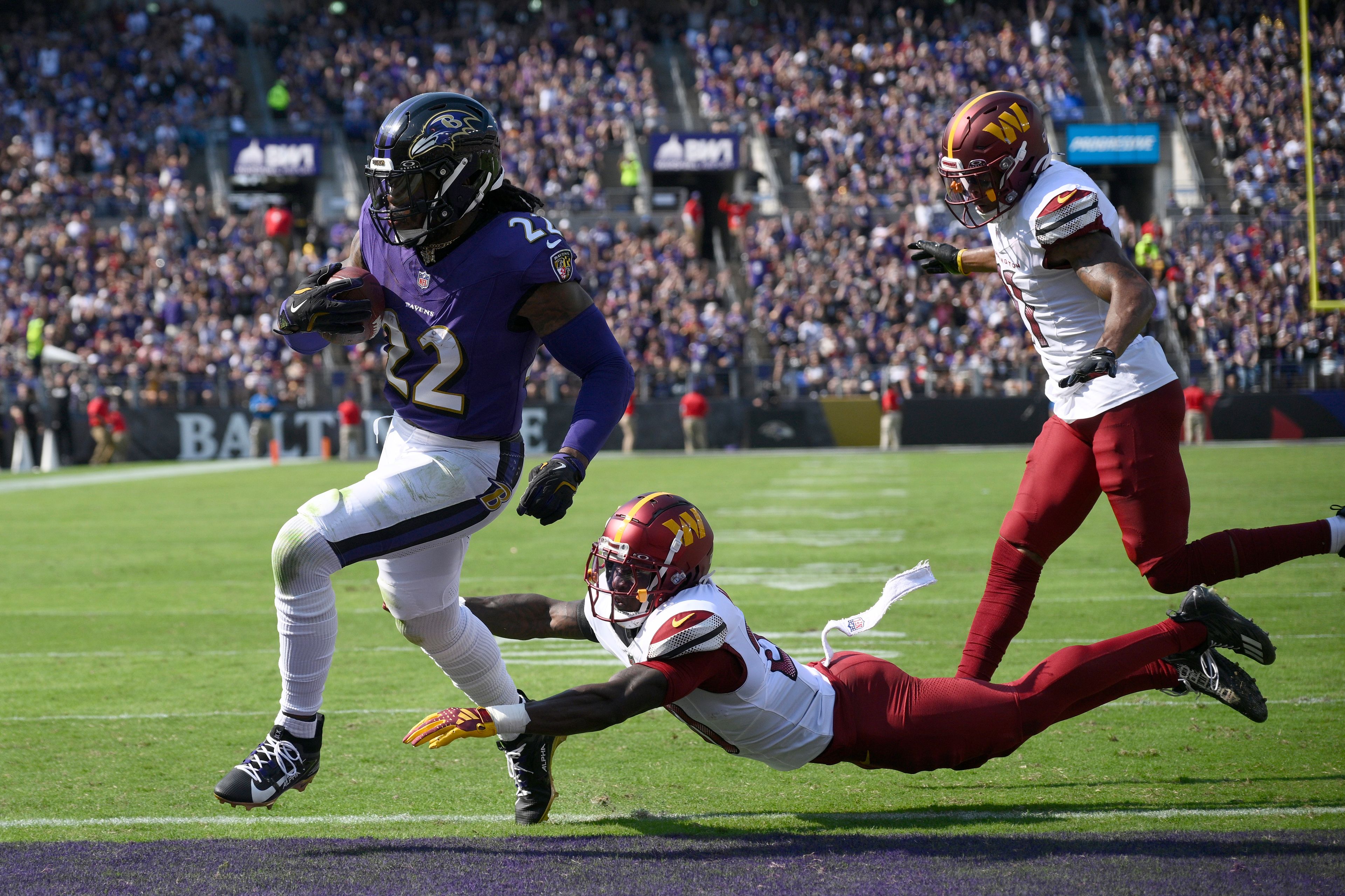 Baltimore Ravens running back Derrick Henry (22) scores past Washington Commanders safety Quan Martin and safety Jeremy Chinn, right, during the first half of an NFL football game Sunday, Oct. 13, 2024, in Baltimore. (AP Photo/Nick Wass)