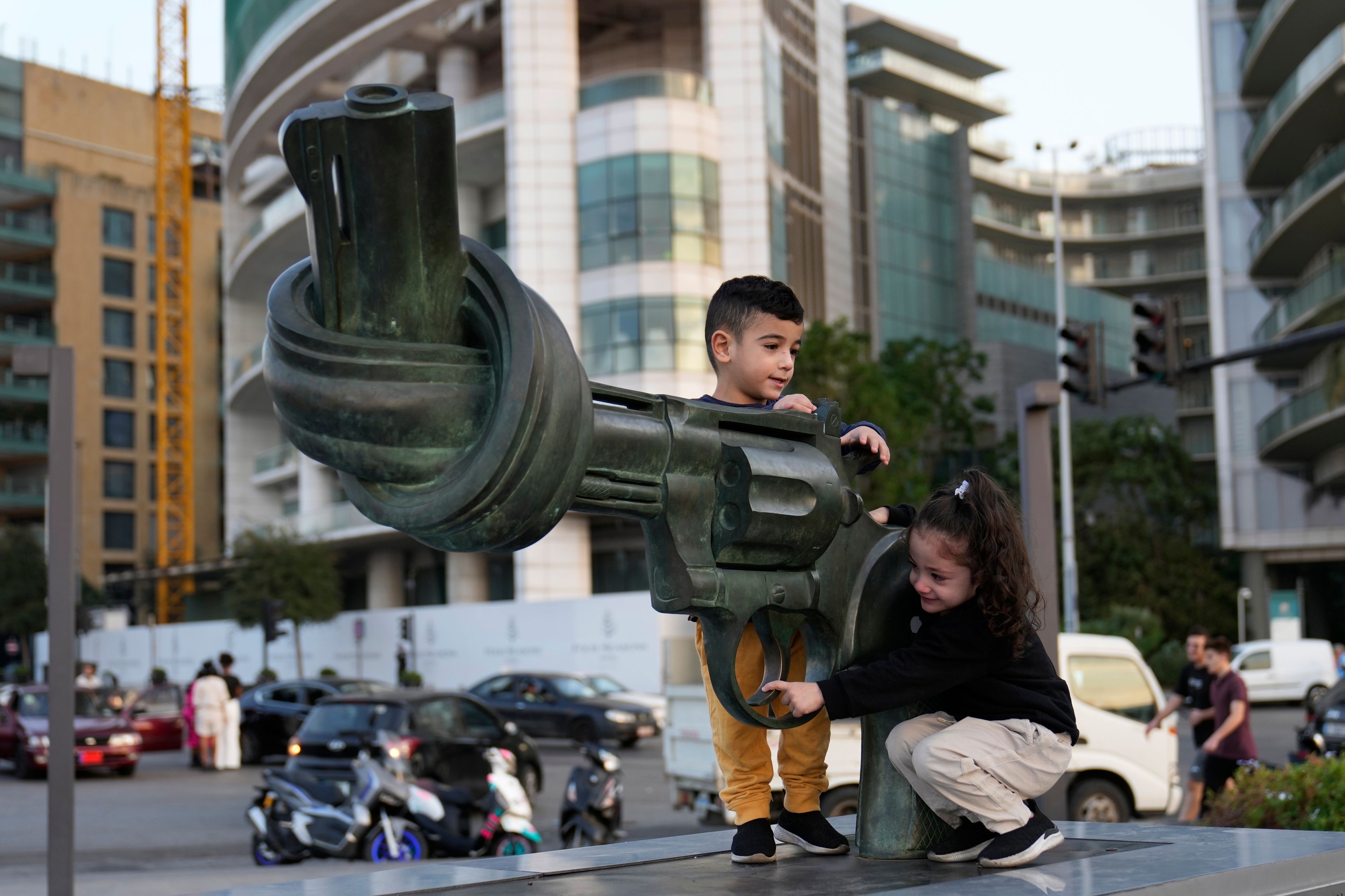 Hussein and Zahraa, 3, displaced Lebanese twins who fled with their parents from their village of Mais al-Jabal in south Lebanon amid the ongoing Hezbollah-Israel war, play on a gun with a twisted barrel statute, symbolizing anti-violence, in Beirut, Lebanon, Thursday, Oct. 31, 2024. (AP Photo/Hussein Malla)