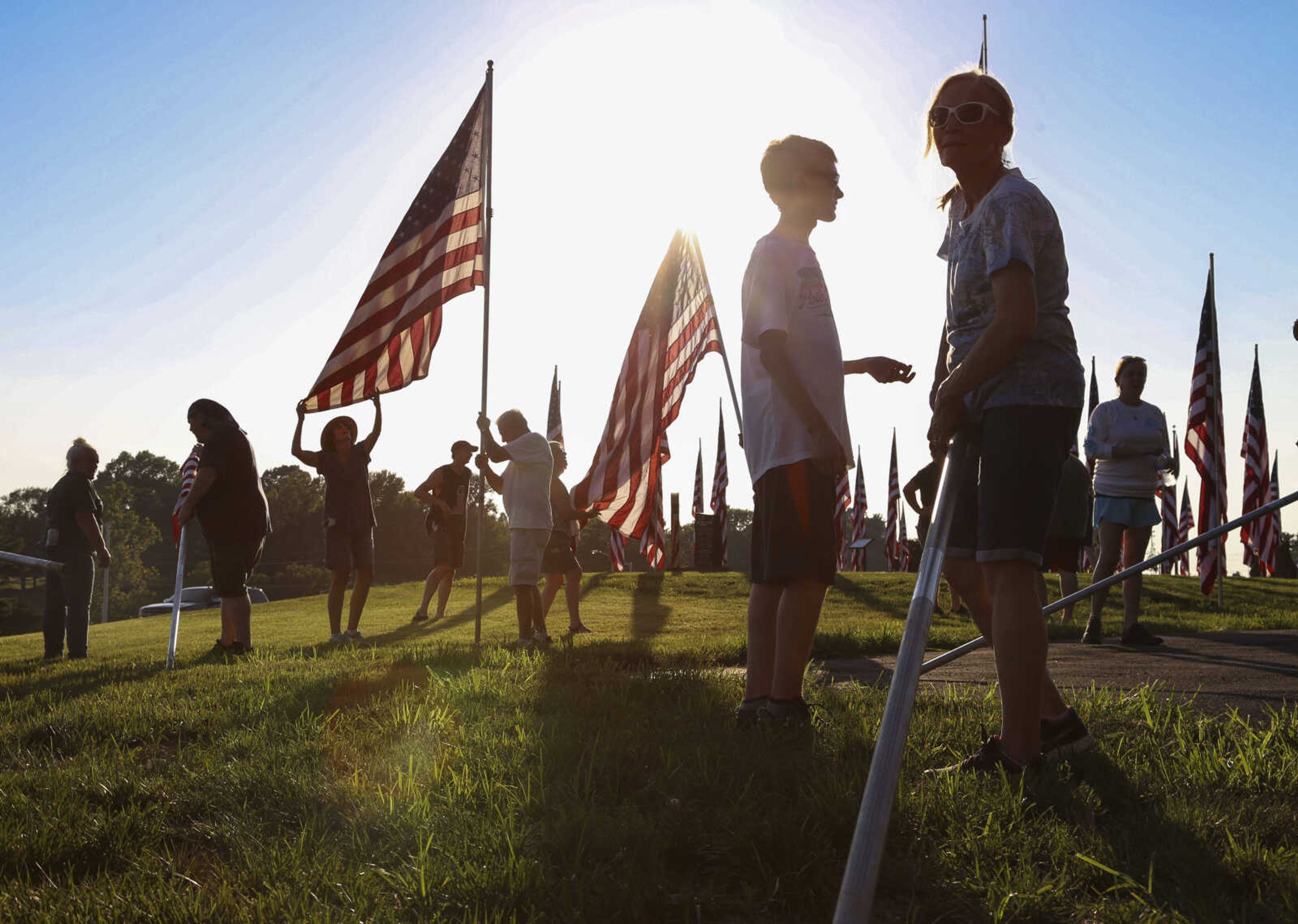 Joyce Bock, front right, of Oak Ridge, holds a rolled flag while taking down the Avenue of Flags with other volunteers Wednesday, July 4, 2018, at Cape County Park North in Cape Girardeau.