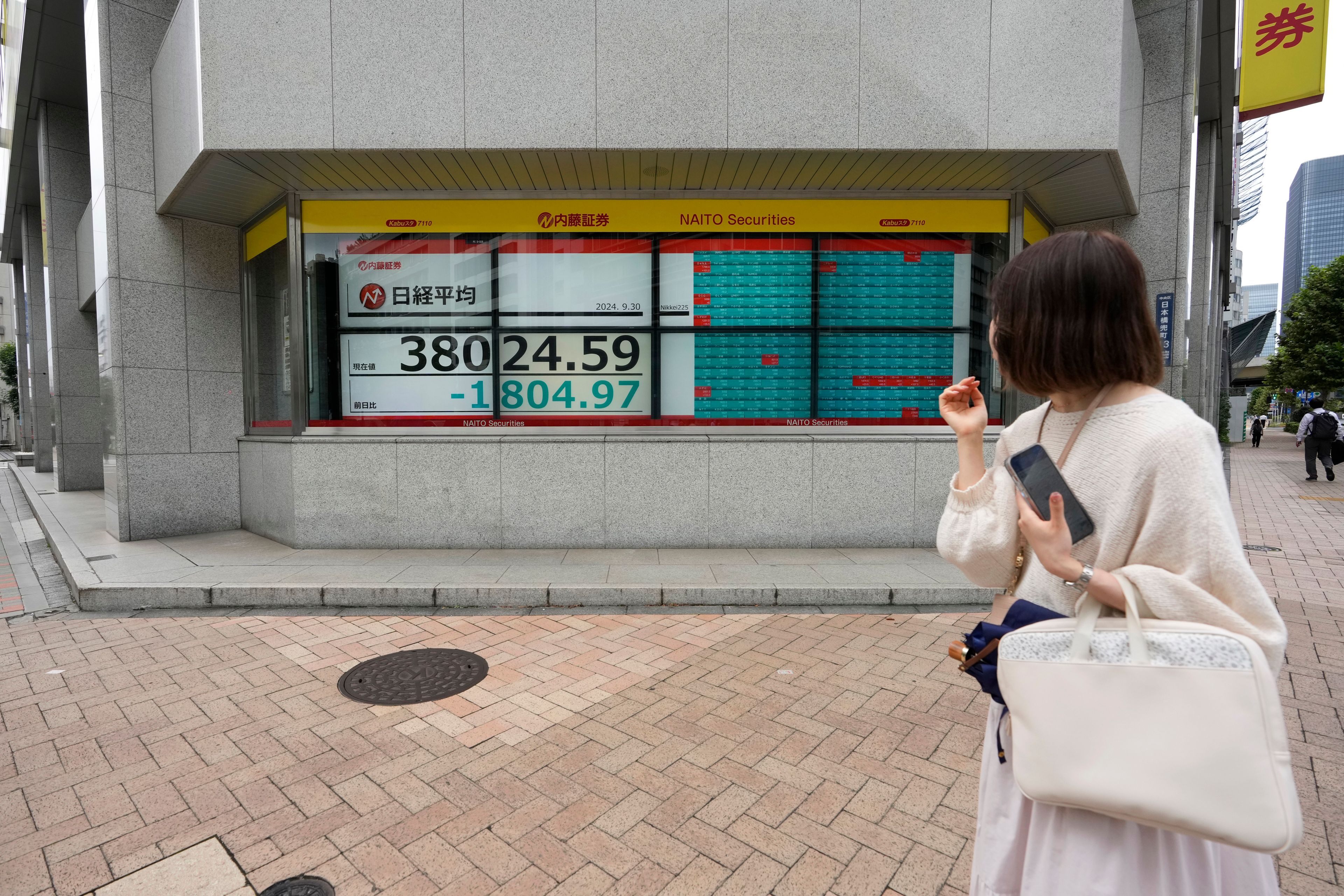 A woman looks at monitors showing Japan's Nikkei 225 index at a securities firm as she waits at an traffic intersection in Tokyo, Monday, Sept. 30, 2024. (AP Photo/Hiro Komae)