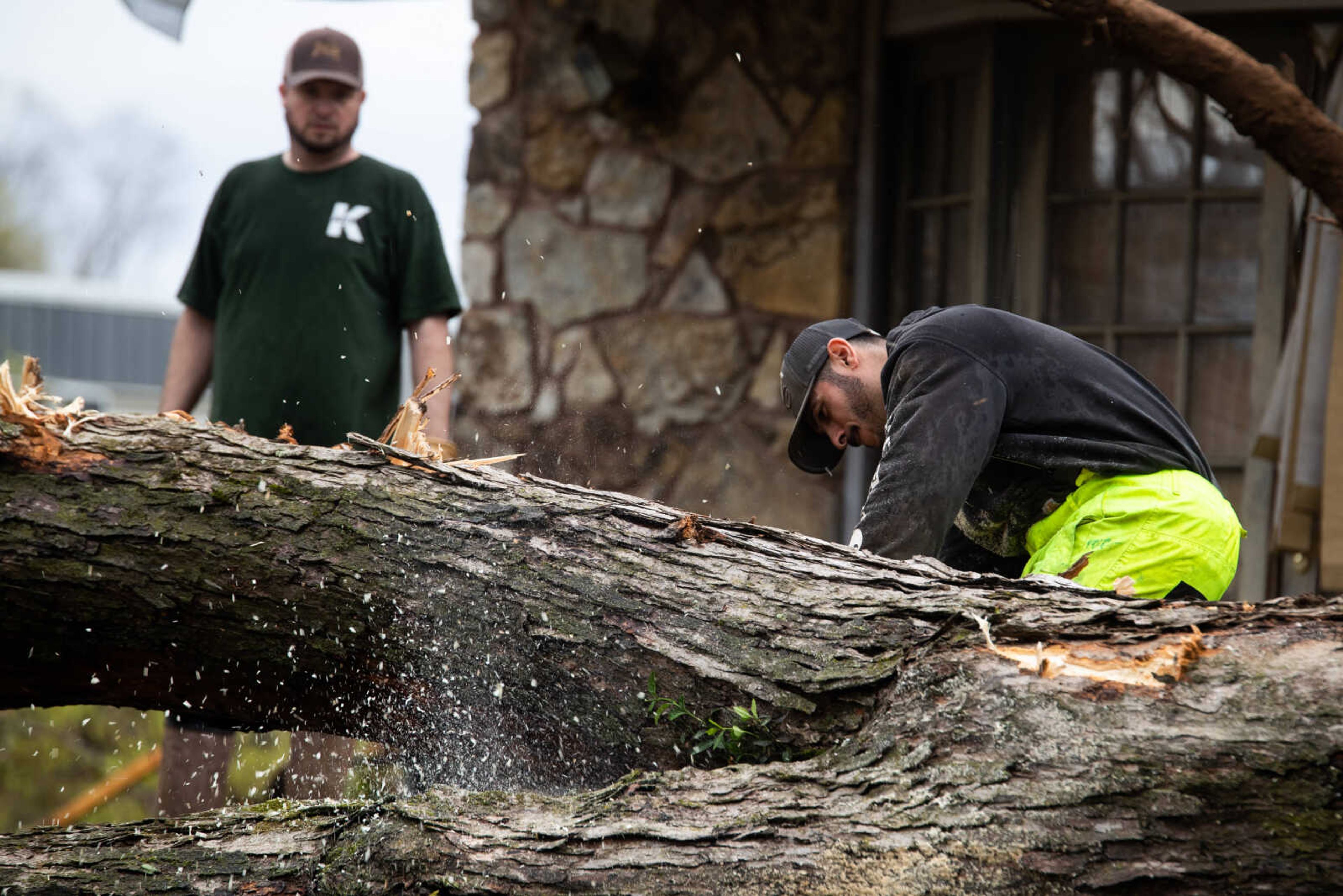 Miguel Echeuarria, right, cuts up a tree with a chainsaw.