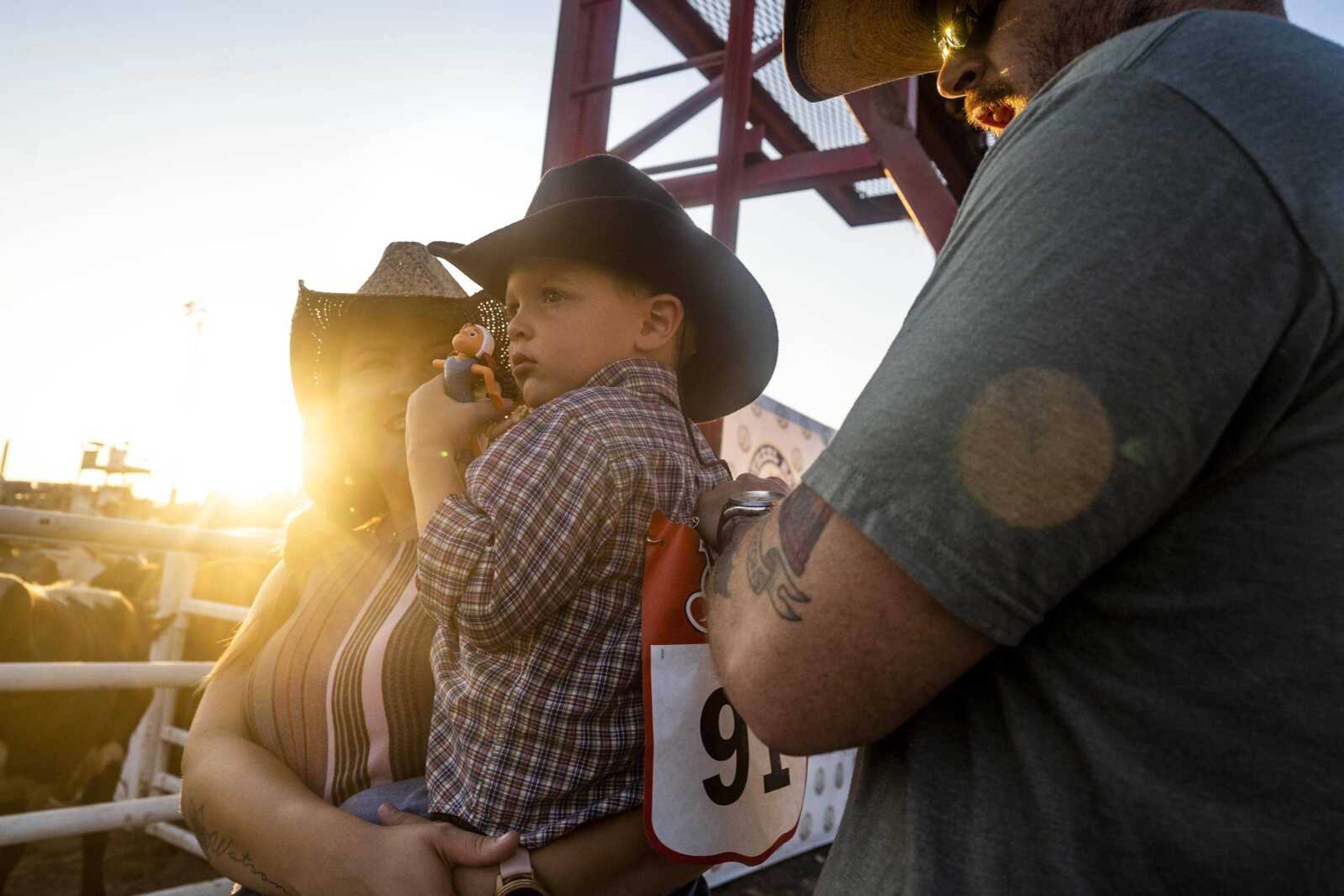 Kelsea Green, far left, laughs as Zechariah Green pins a rider number on three-year-old Watson Green after receiving the number from a cowboy near an exit chute during the first night of the Sikeston Jaycee Bootheel Rodeo on Wednesday, Aug. 11, 2021, in Sikeston, Missouri.