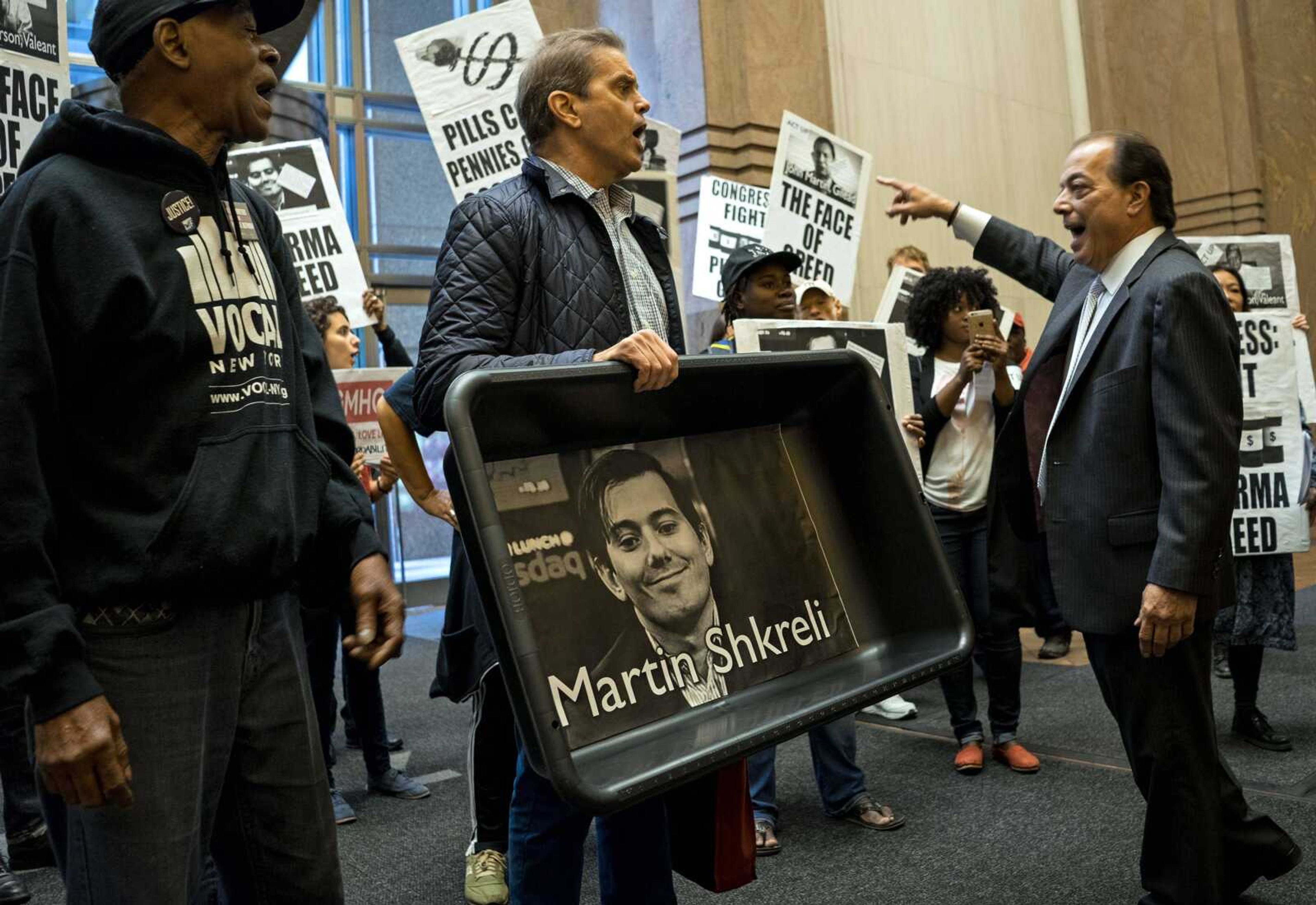 AIDS activists and others, including one carrying an image of Turing Pharmaceuticals CEO Martin Shkreli in a makeshift cat-litter pan, are asked to leave a New York City hotel lobby during a protest Oct. 1 highlighting pharmaceutical drug pricing. (Craig Ruttle ~ Associated Press)