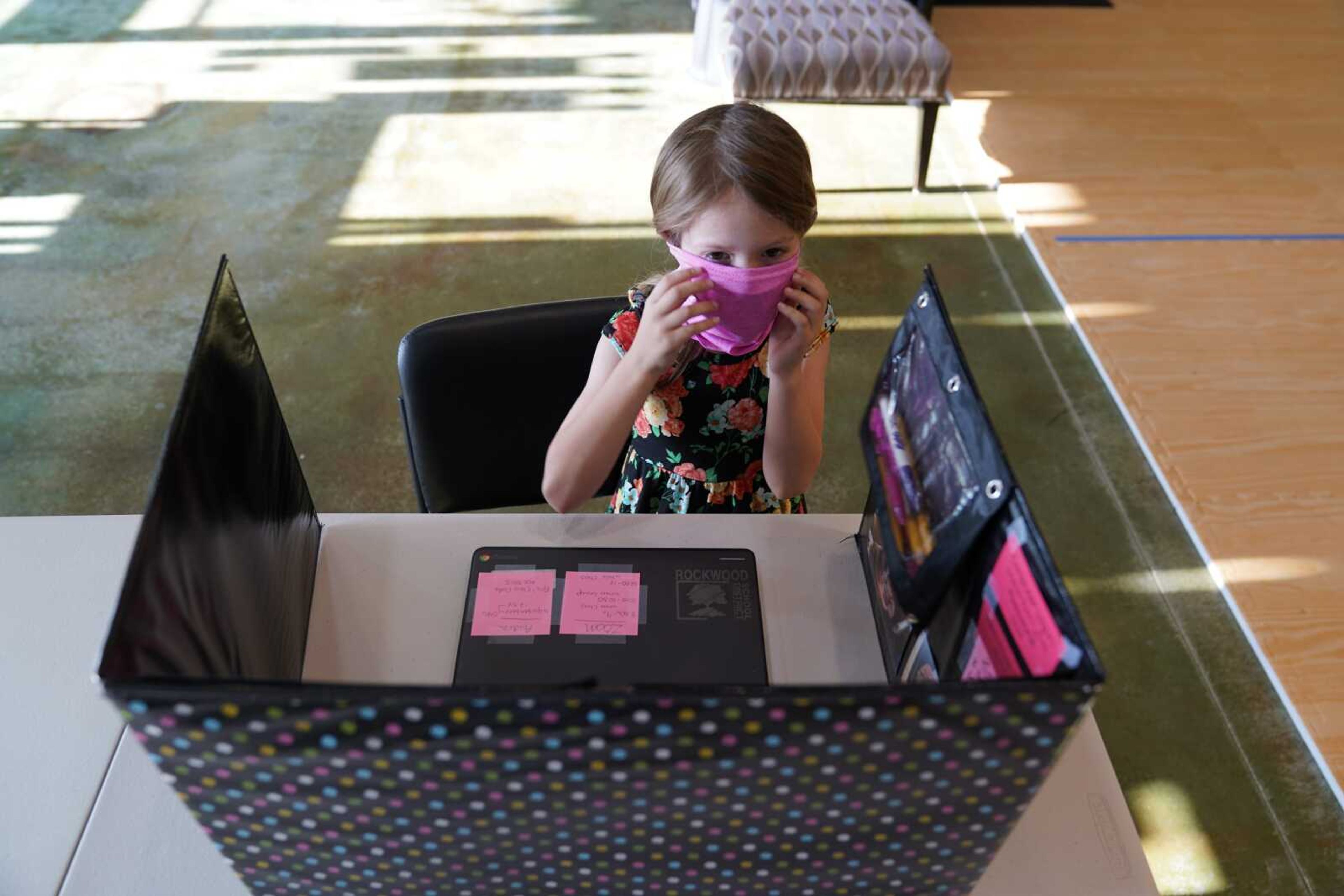 Audra Quisenberry, 6, puts on a mask as she sits at her desk inside Premier Martial Arts on her first day of school Monday in Wildwood, Missouri. The first-grader will attend her classes virtually while spending her days at the martial arts studio since her school has been shutdown due to the COVID-19 outbreak.