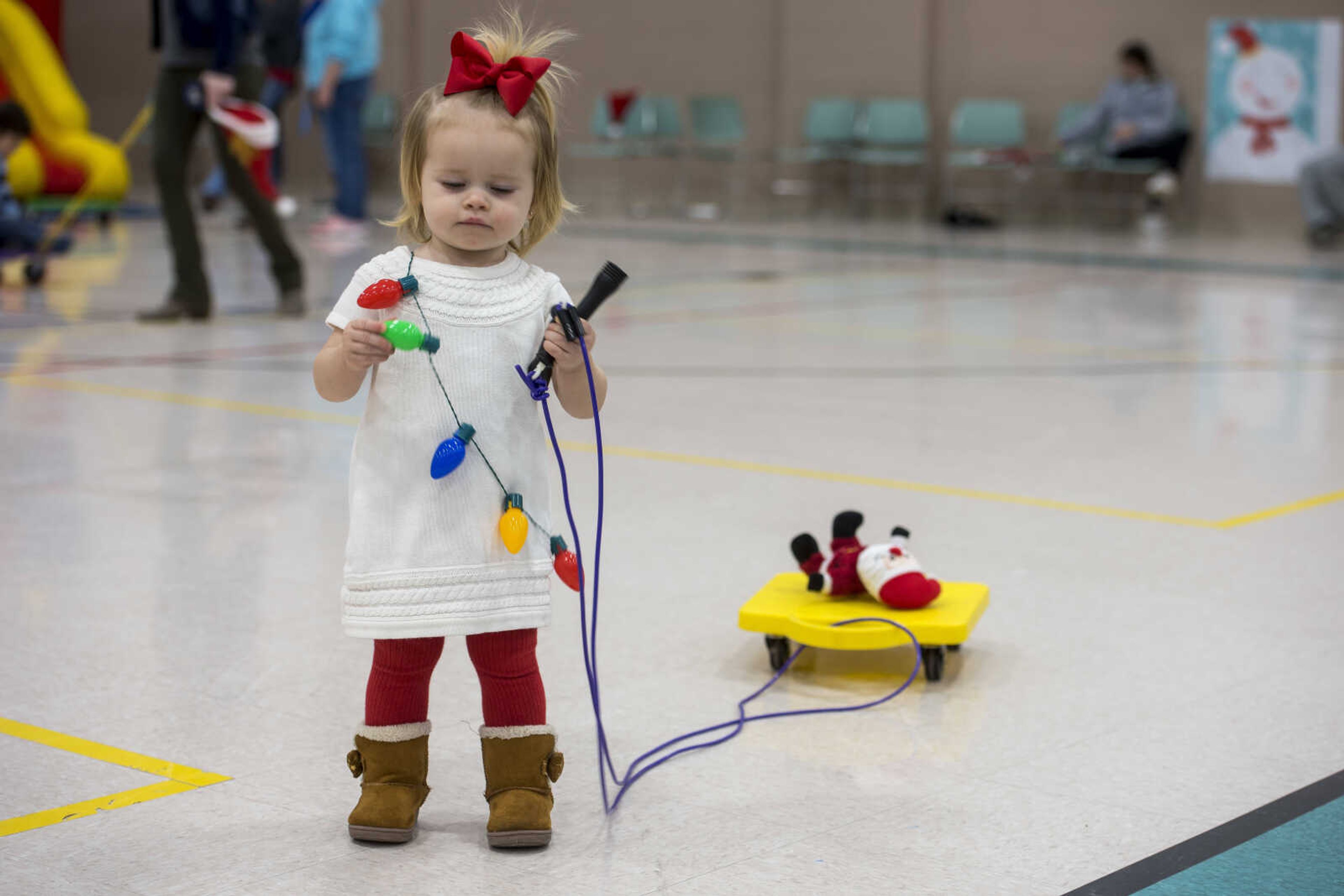 Berkley Dennis, 1, leads her Santa Claus doll around on a scooter board during a family breakfast with Santa Claus at the Osage Center Saturday, Dec. 15, 2018.