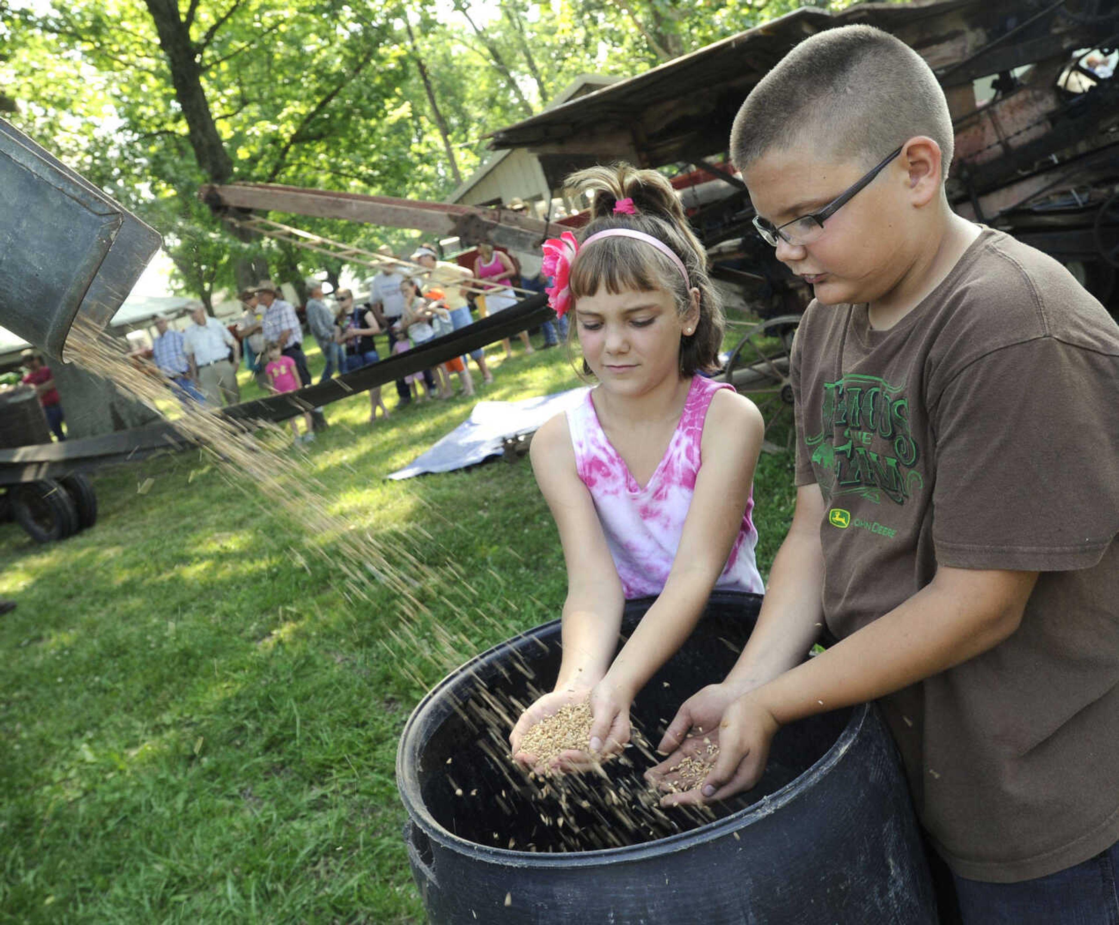 Molly Conrad and Matthew Conrad of Sedgewickville, Mo. grab some wheat from Willard Hadler's 1935 Case thresher Saturday at Old Timers' Day in Perryville, Mo.