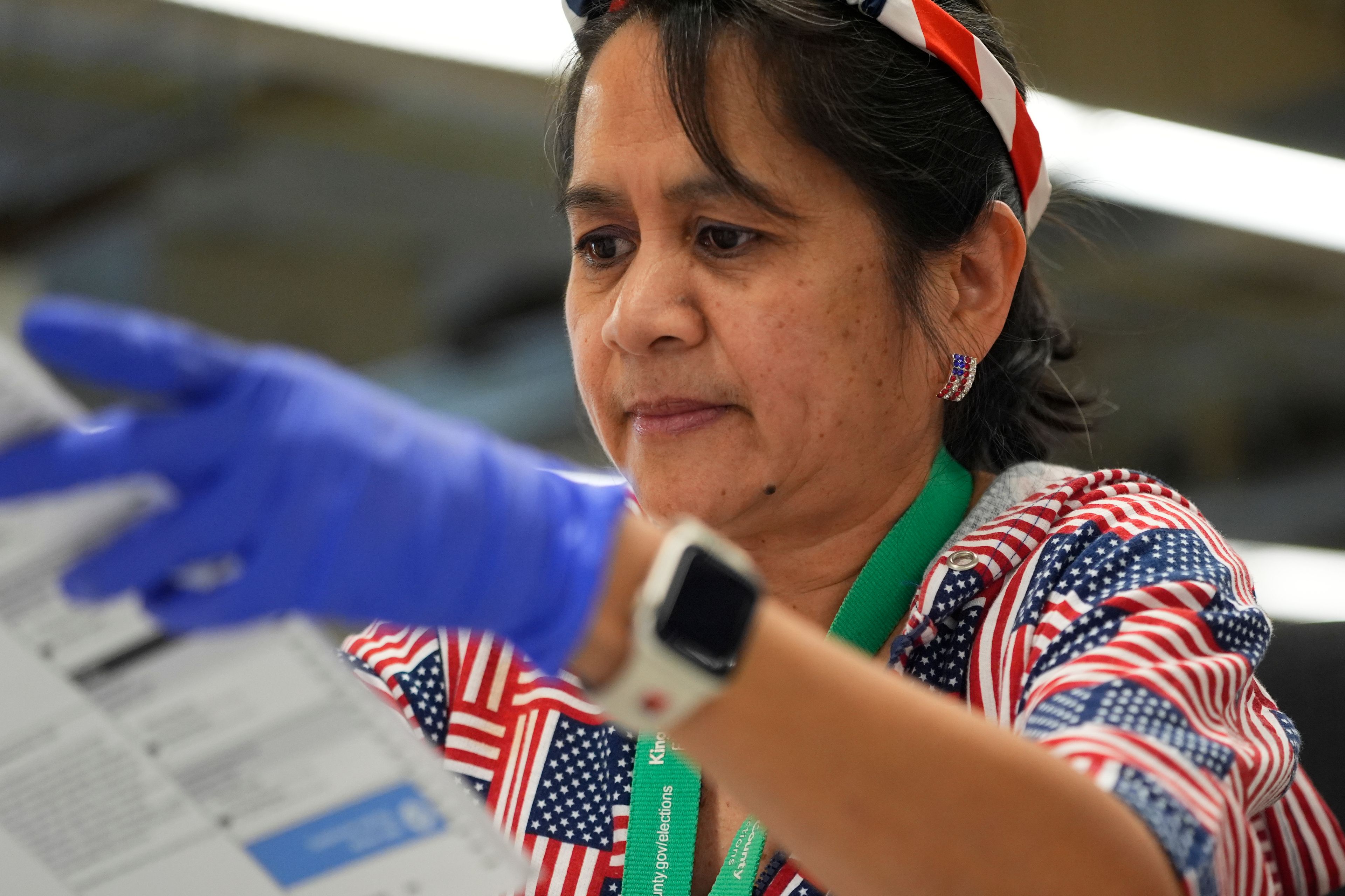 Evangeline Hebron wears an American flag headband, earrings and shirt while opening ballots to prepare for counting at King County Elections headquarters on Election Day, Tuesday, Nov. 5, 2024, in Renton, Wash. (AP Photo/Lindsey Wasson)