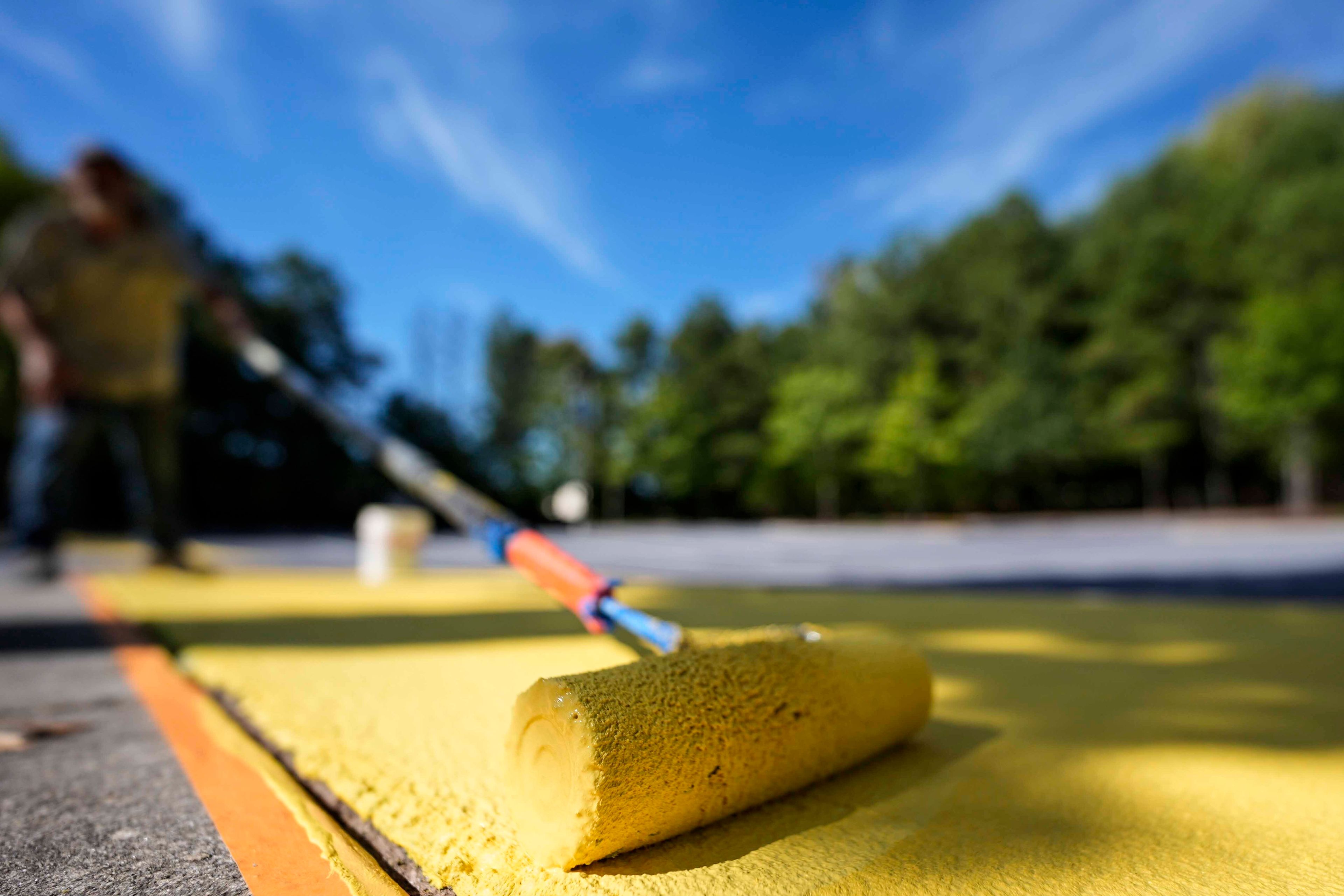 Ronnie Jefferies paints the parking lot at Science, Arts and Entrepreneurship School to help cool it by making it more reflective, Wednesday, Sept. 4, 2024, in Mableton, Ga. (AP Photo/Mike Stewart)