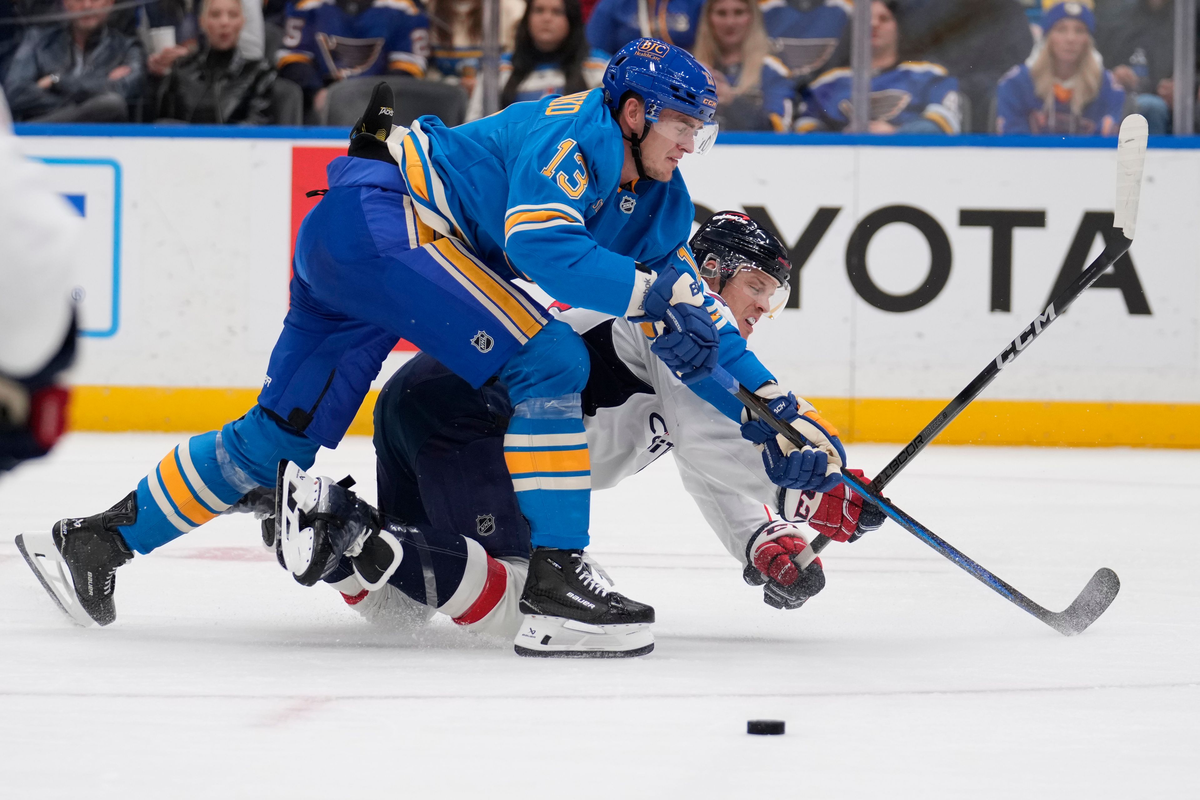 St. Louis Blues' Alexey Toropchenko (13) and Washington Capitals' John Carlson battle for a loose puck during the second period of an NHL hockey game Saturday, Nov. 9, 2024, in St. Louis. (AP Photo/Jeff Roberson)