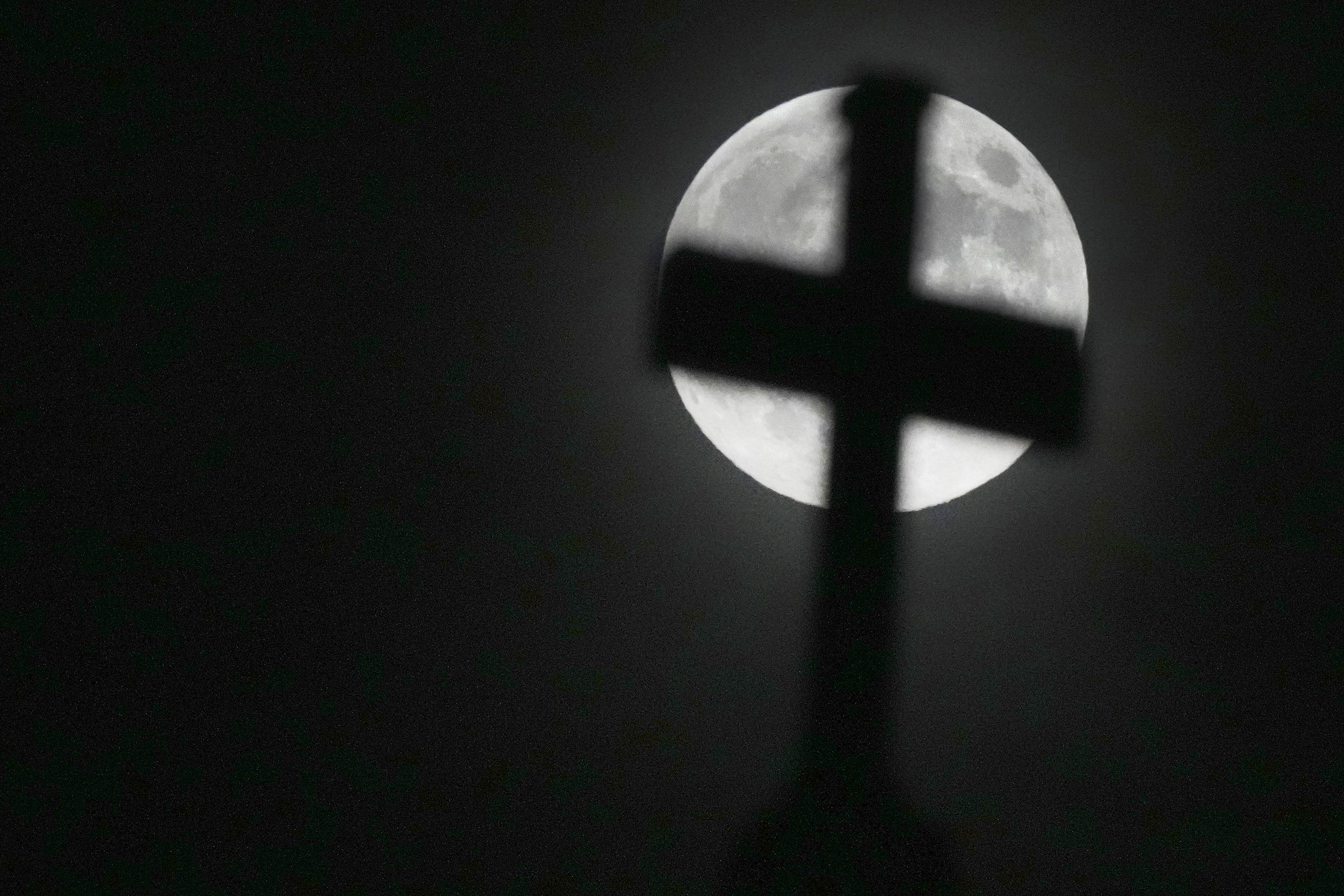 The moon rises behind the cross on top of St Paul's Church in Ealing, London, Friday, Nov. 15, 2024. (AP Photo/Frank Augstein)