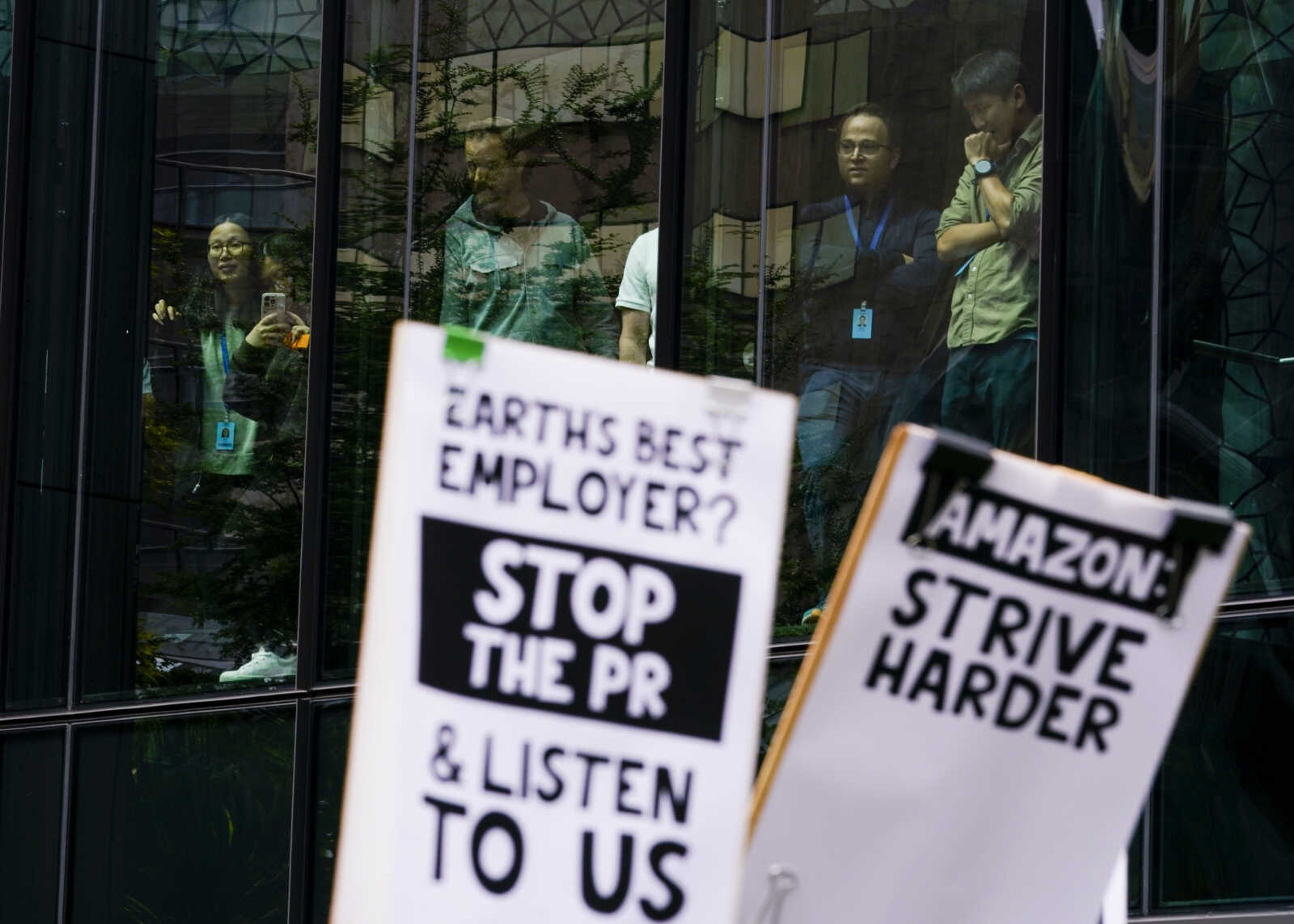 Amazon employees watch from a staircase in the Day 1 building as other corporate workers hold picket signs while participating in a walkout to protest the company's return-to-office policies, Wednesday, May 31, 2023, in Seattle. Organizers called attention to the climate impact of commutes, saying it runs counter to the company s  Climate Pledge  to be carbon neutral by the year 2040, as well as concerns about recent layoffs. (AP Photo/Lindsey Wasson)