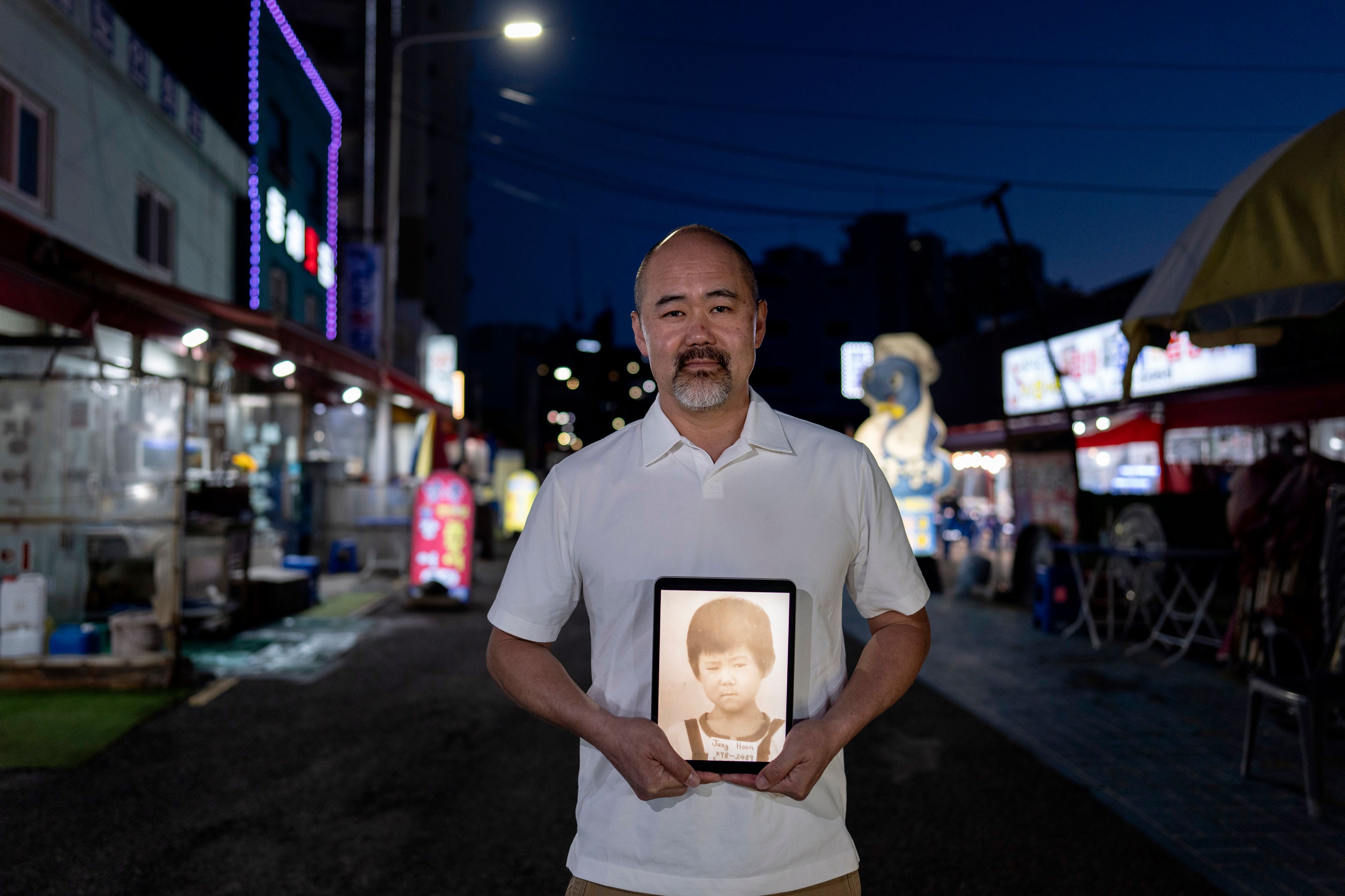 Kenneth Barthel, adopted from South Korea to Hawaii in 1979 at 6 years old, holds a tablet showing his childhood photo in Busan, South Korea, Thursday, May 16, 2024. Barthel is looking for his birth family in Busan where he believes he was abandoned when his mother ordered soup for him in a restaurant and never returned. (AP Photo/Jae C. Hong)