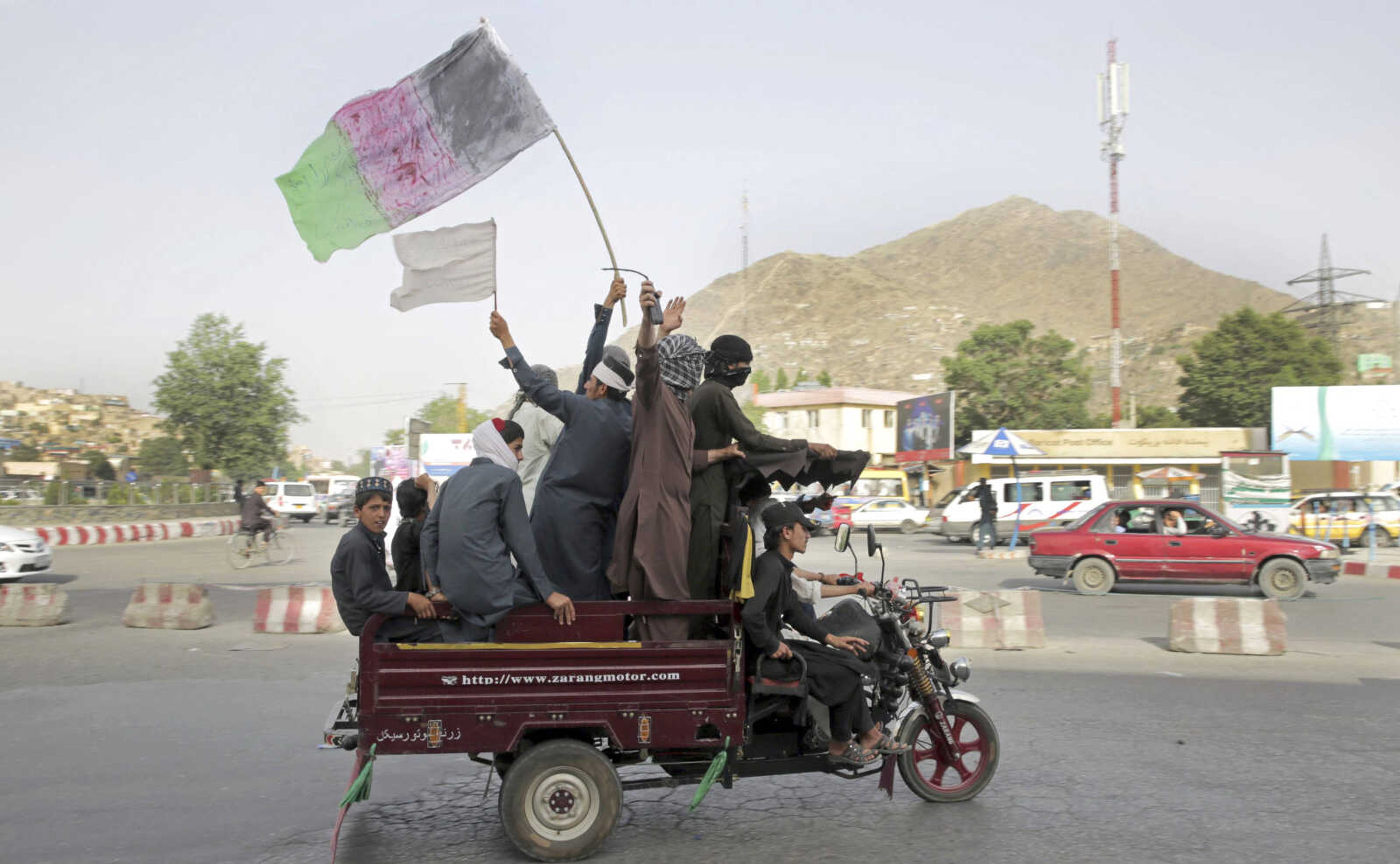 Taliban fighters and their supporters carry a representation of the Afghan national flag and a Taliban flag Sunday while riding in a motorized vehicle, in Kabul, Afghanistan.