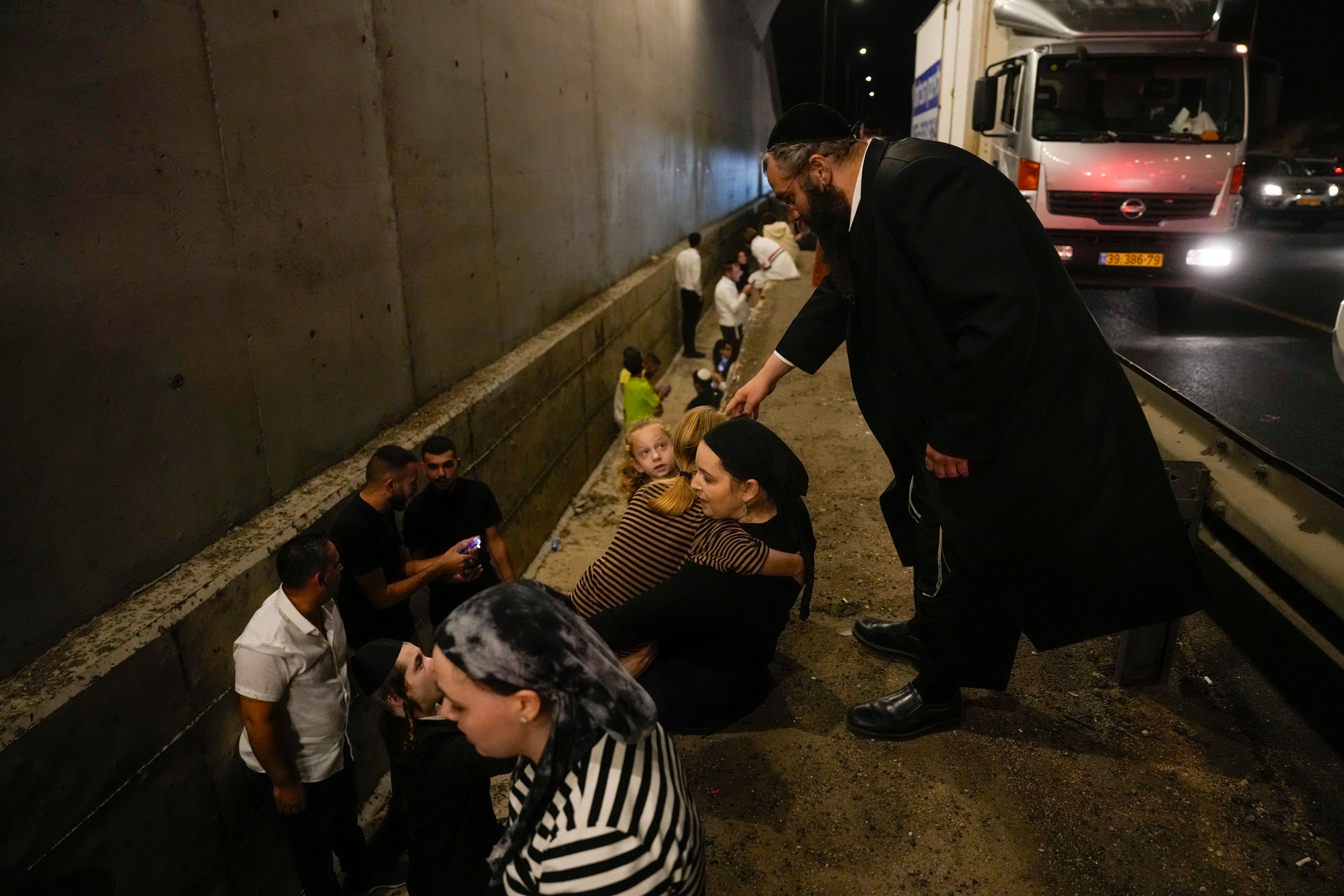 People take cover on the side of a road as a siren sounds a warning of incoming missiles fired from Iran on a freeway in Shoresh, between Jerusalem and Tel Aviv in Israel Tuesday, Oct. 1, 2024. (AP Photo/Ohad Zwigenberg)