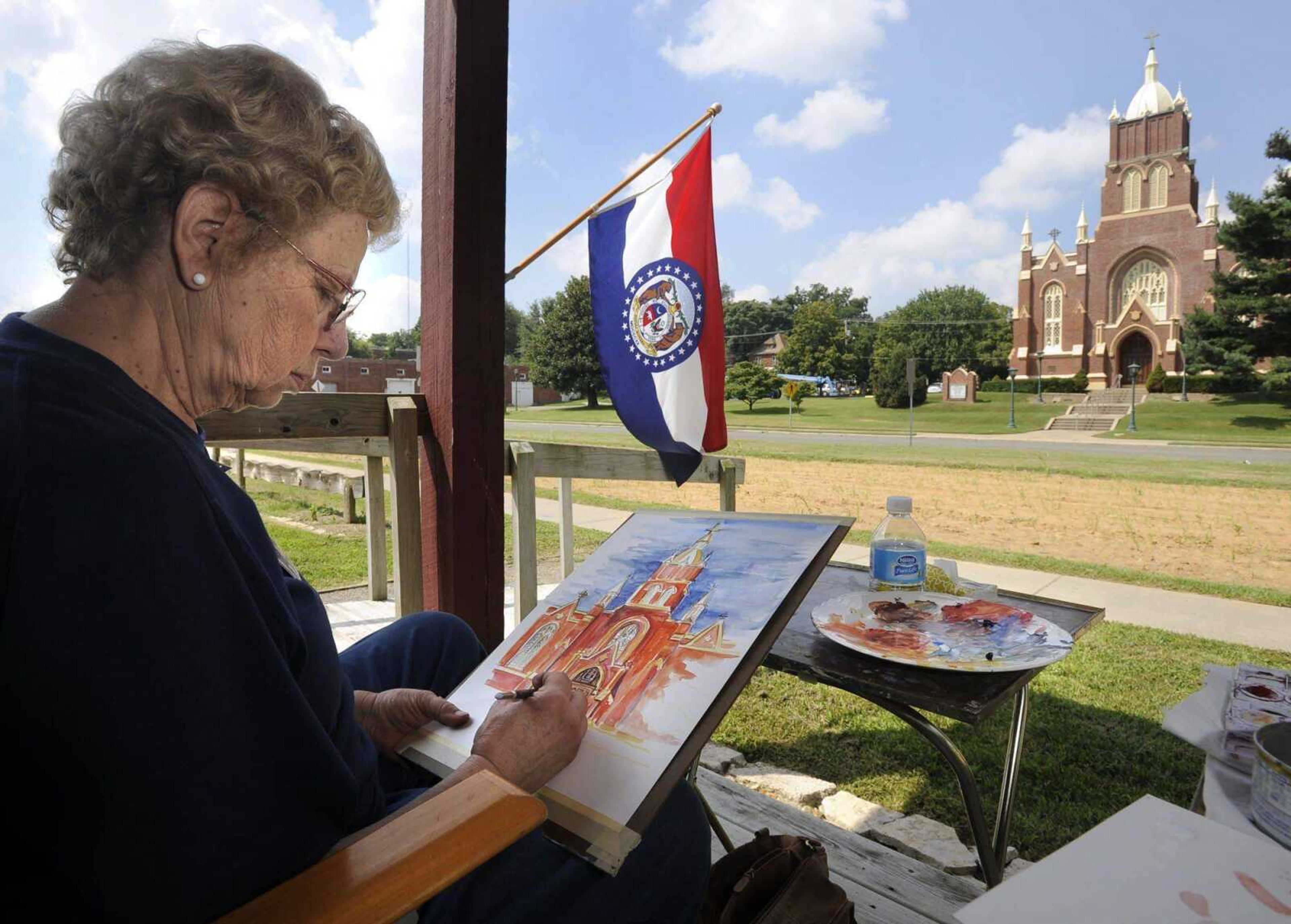 Anita Dickerson works on a watercolor of Old St. Vincent&#8217;s Church on Saturday on the front porch of the Red House Interpretive Center in Cape Girardeau. The center is beside Murtaugh Park, which is being enlarged by filling in the former Aquamsi Street. (Fred Lynch)