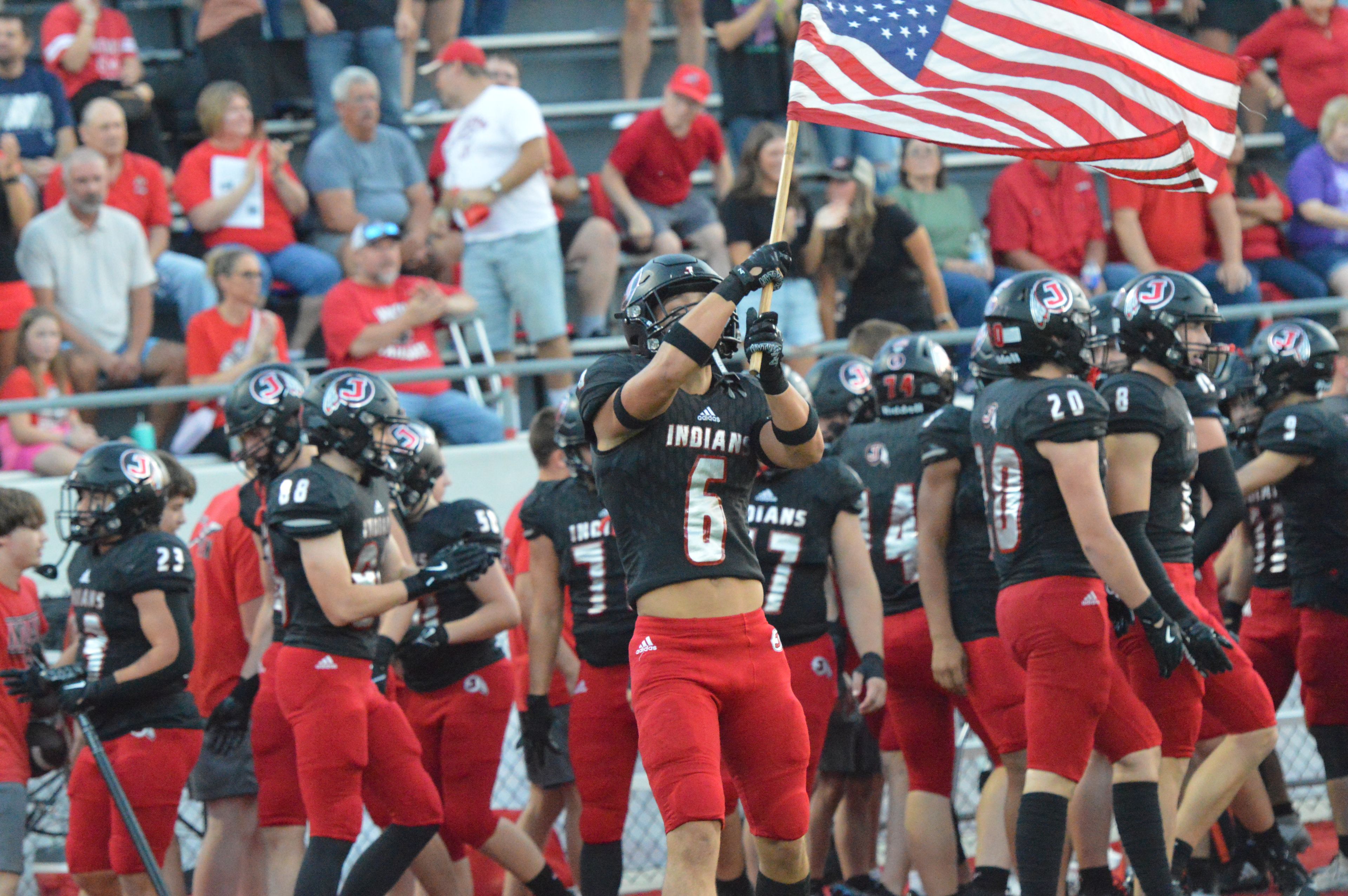 Jackson senior defensive back Gavin Alspaugh waves the American flag during pregame introductions in the home opener against Farmington on Friday, Sept. 20.