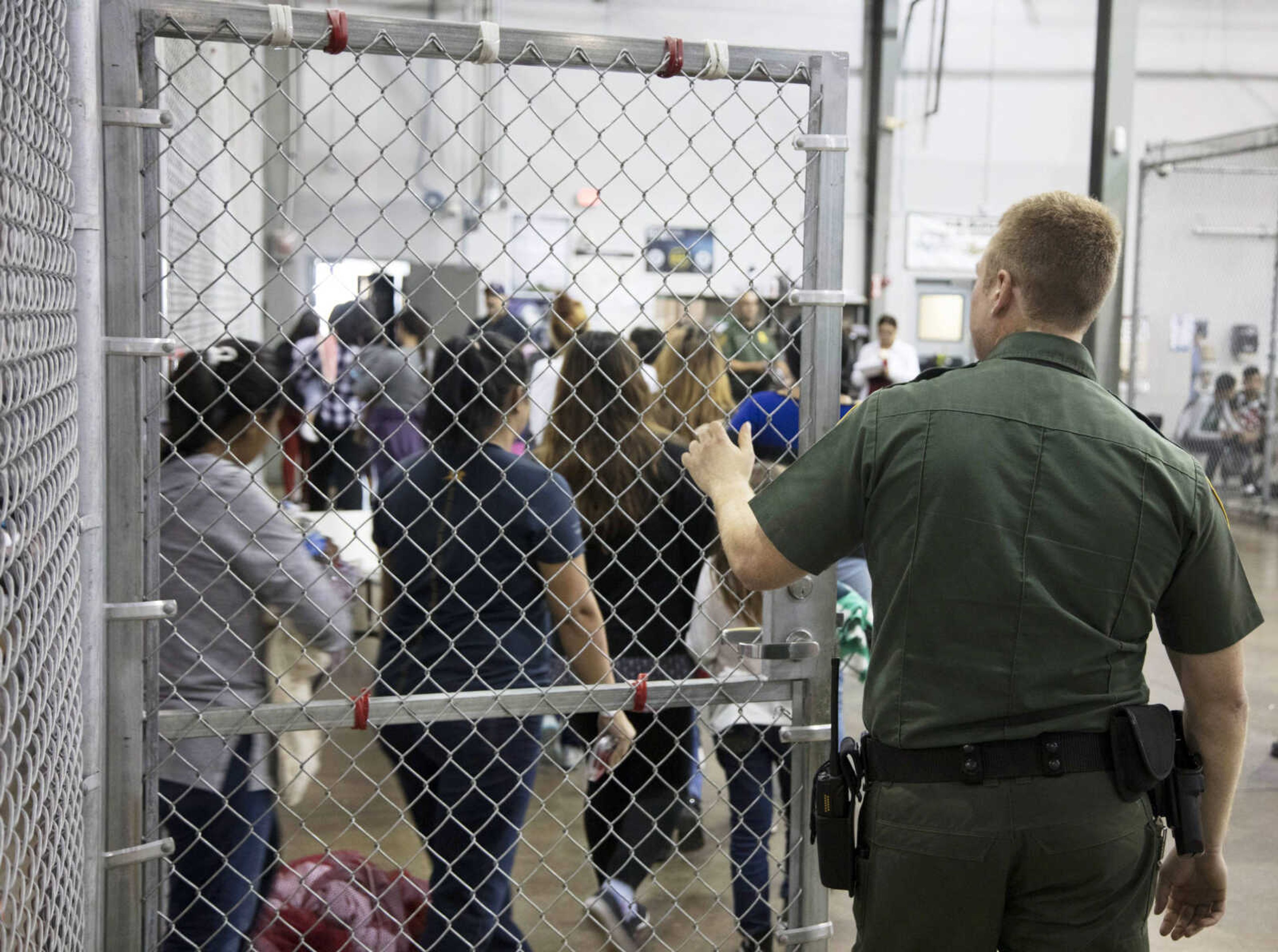 In this photo, a U.S. Border Patrol agent watches as people who've been taken into custody related to cases of illegal entry into the United States stand in line Sunday at a facility in McAllen, Texas.