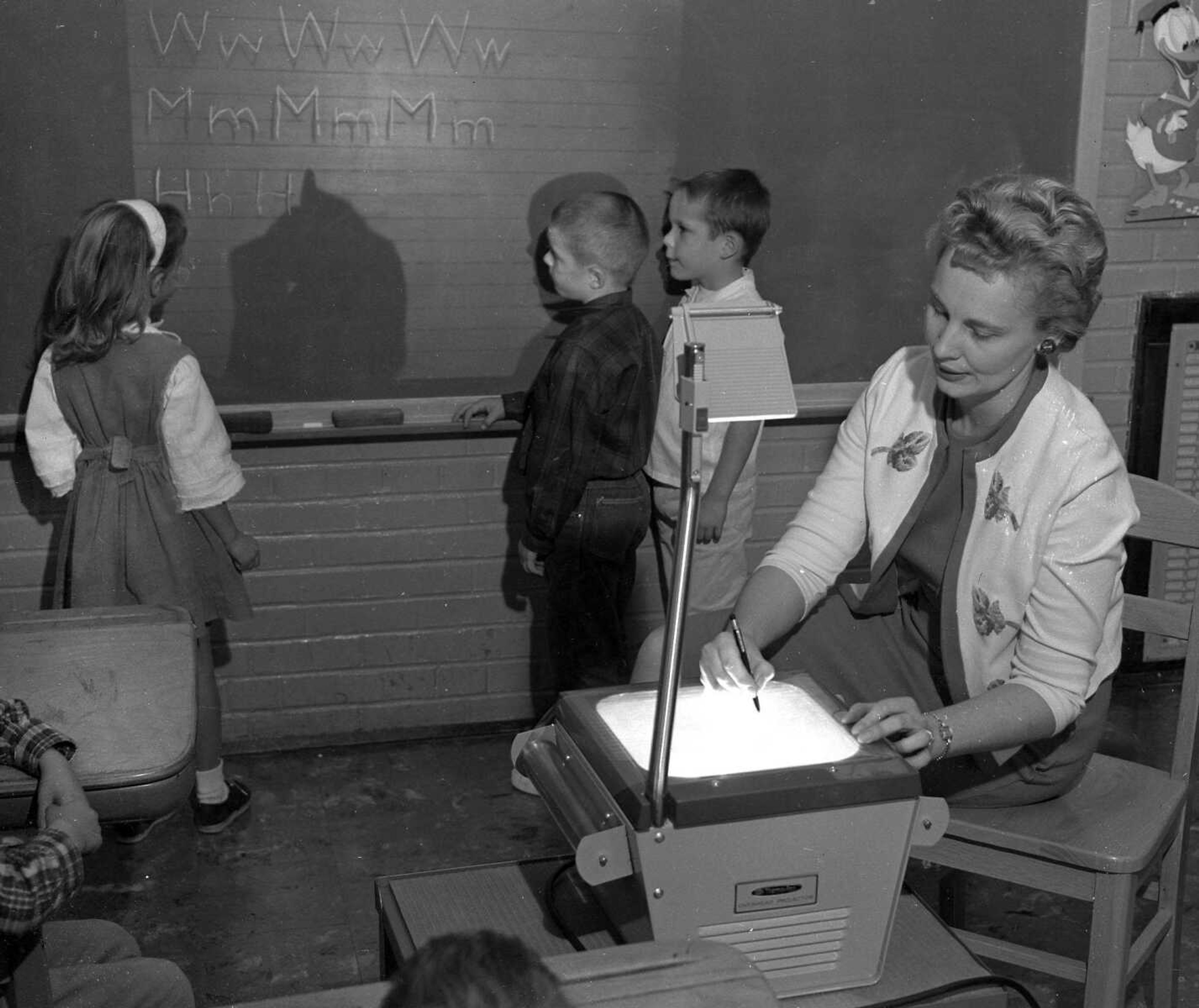 Nov. 16, 1963 Southeast Missourian.
Mrs. Violet Heuer, first grade teacher at Franklin School, uses an overhead projector as her students practice manuscript writing on the board, from left, Sheila Hale, Mike Kembel and Wayne Hutchison. (G.D. Fronabarger/Southeast Missourian archive)
[A similar picture was published along with a story.]