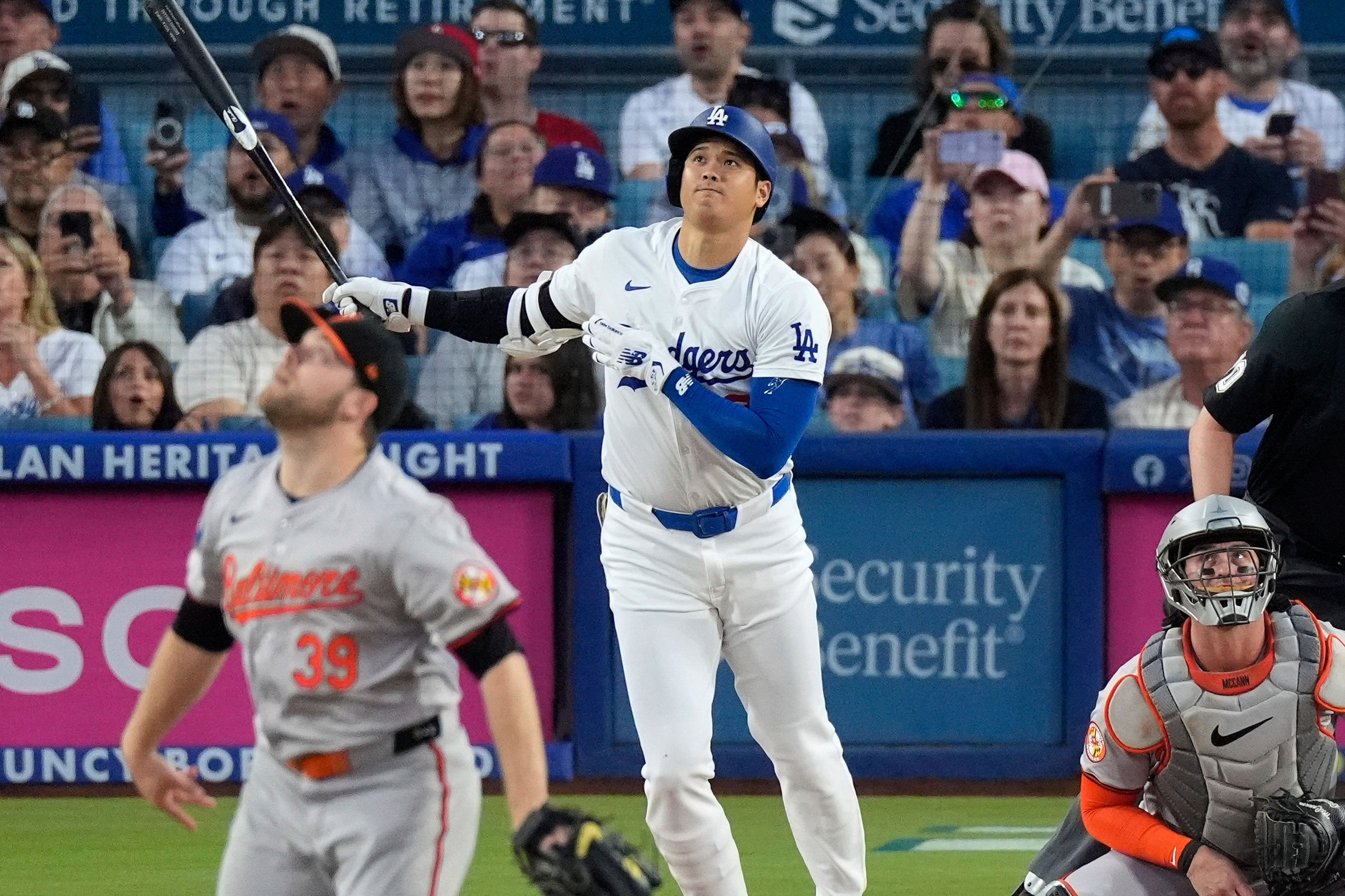 Los Angeles Dodgers' Shohei Ohtani, center, hits a solo home run as Baltimore Orioles starting pitcher Corbin Burnes, left, and catcher James McCann, right, watch during the first inning of a baseball game Wednesday, Aug. 28, 2024, in Los Angeles. (AP Photo/Mark J. Terrill)