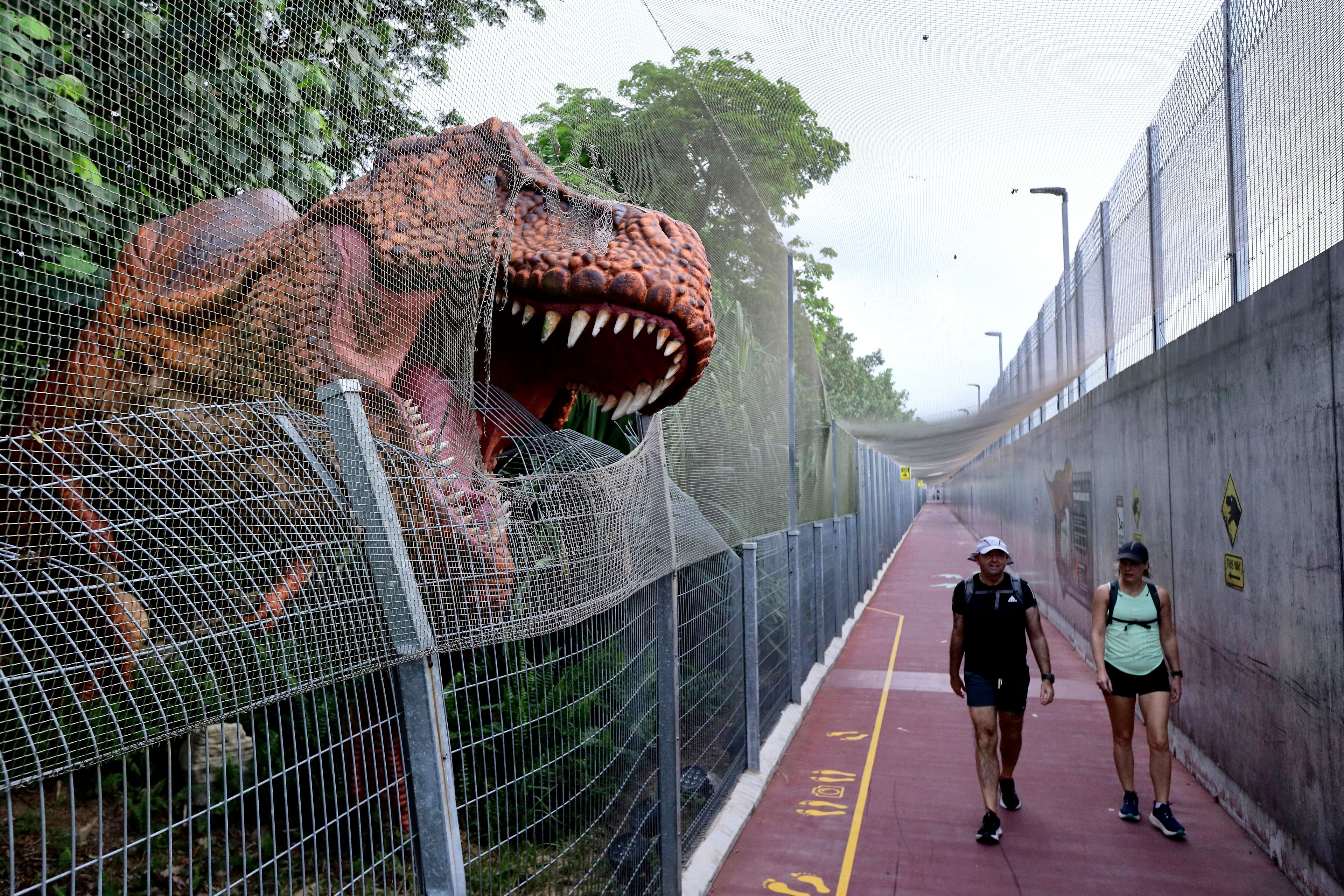 People walk past past a life size dinosaur replica along the Changi Jurassic Mile in Singapore, Sunday, Sept. 8, 2024. (AP Photo/Suhaimi Abdullah)