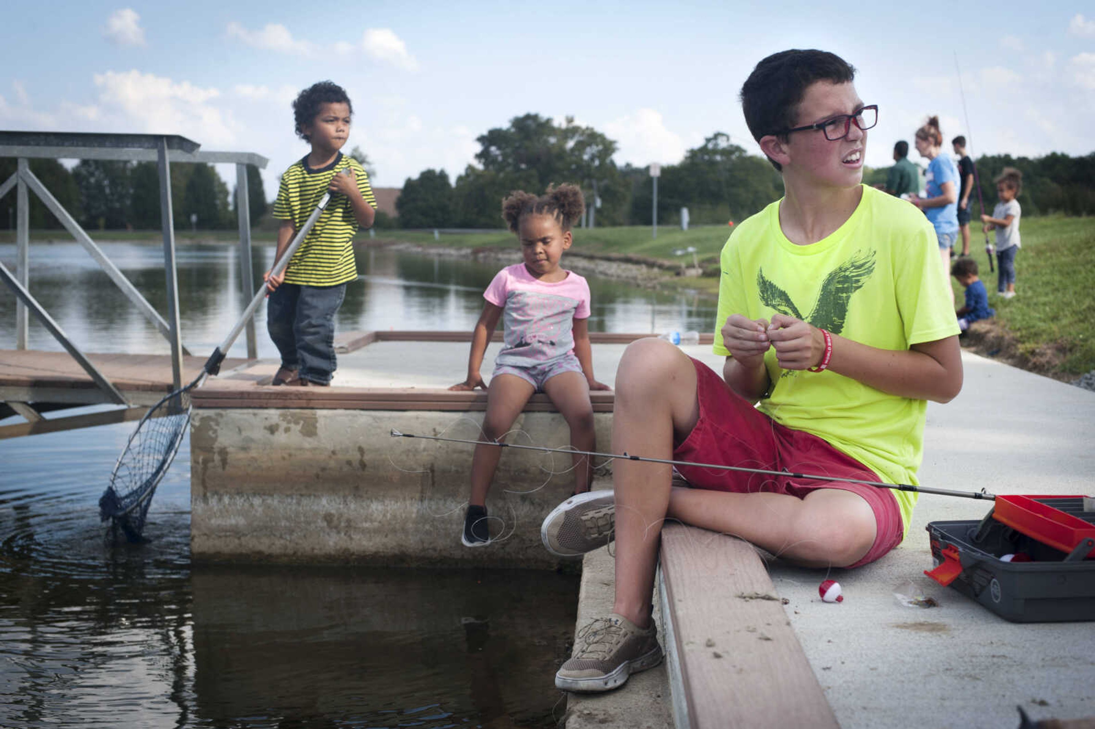 Austin Collins, 13, baits his line while sitting on the dock with 4-year-old Essence Barnett, center, as 4-year-old Zeydrian Wade attempts to catch fish with a net Sept. 29, 2019, at Cape County Park North.