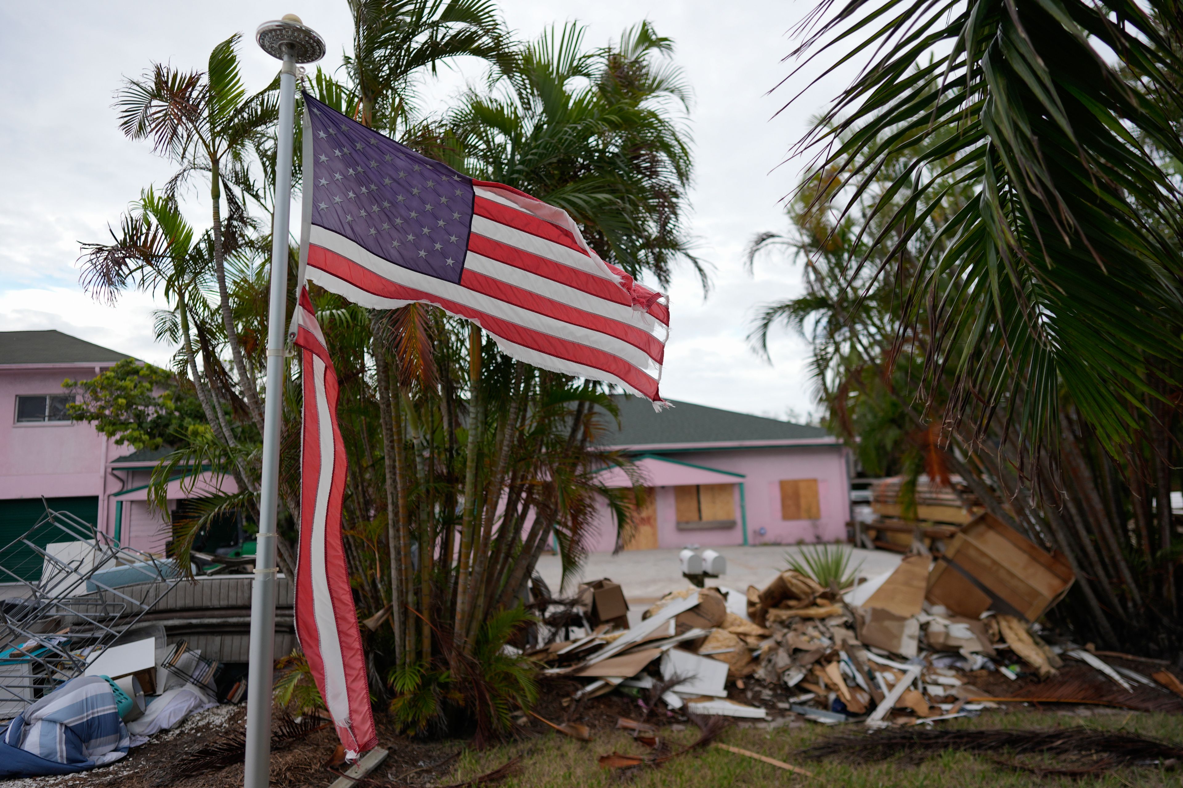 A tattered American flag flaps outside a home as furniture and household items damaged by Hurricane Helene flooding sit piled along the street awaiting pickup, ahead of the arrival of Hurricane Milton, in Holmes Beach on Anna Maria Island, Fla., Tuesday, Oct. 8, 2024. (AP Photo/Rebecca Blackwell)