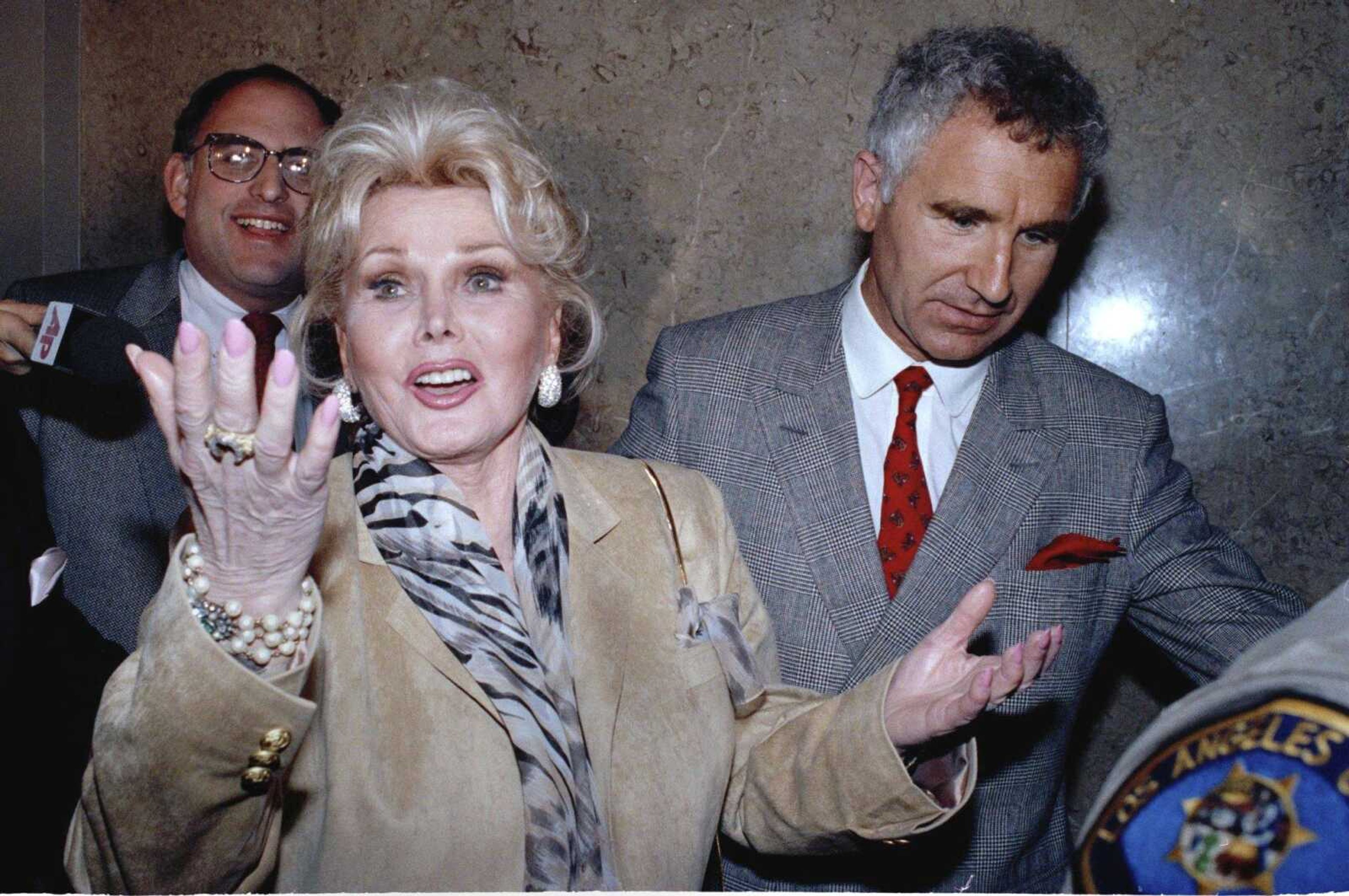 Zsa Zsa Gabor gestures as she leaves the Beverly Hills courtroom where judge Charles Rubin ruled she violated her probation May 1, 1990. At right is her husband, Frederick von Anhalt.