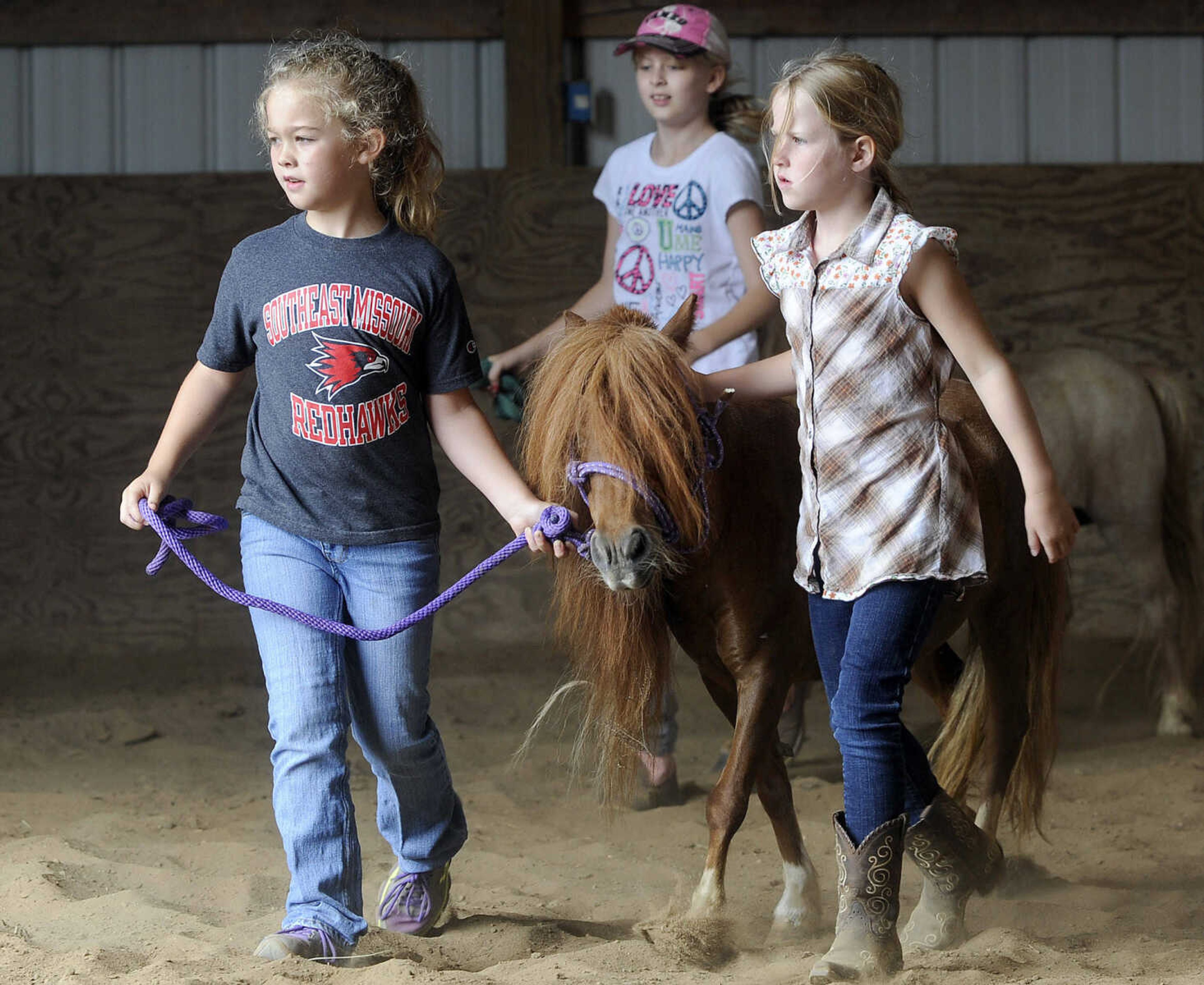 Emma Benton, left, and Vivian Nordin walk with Sierra in the barn at a horseback riding camp Monday, July 6, 2015 at Rolling Hills Farm west of Cape Girardeau.