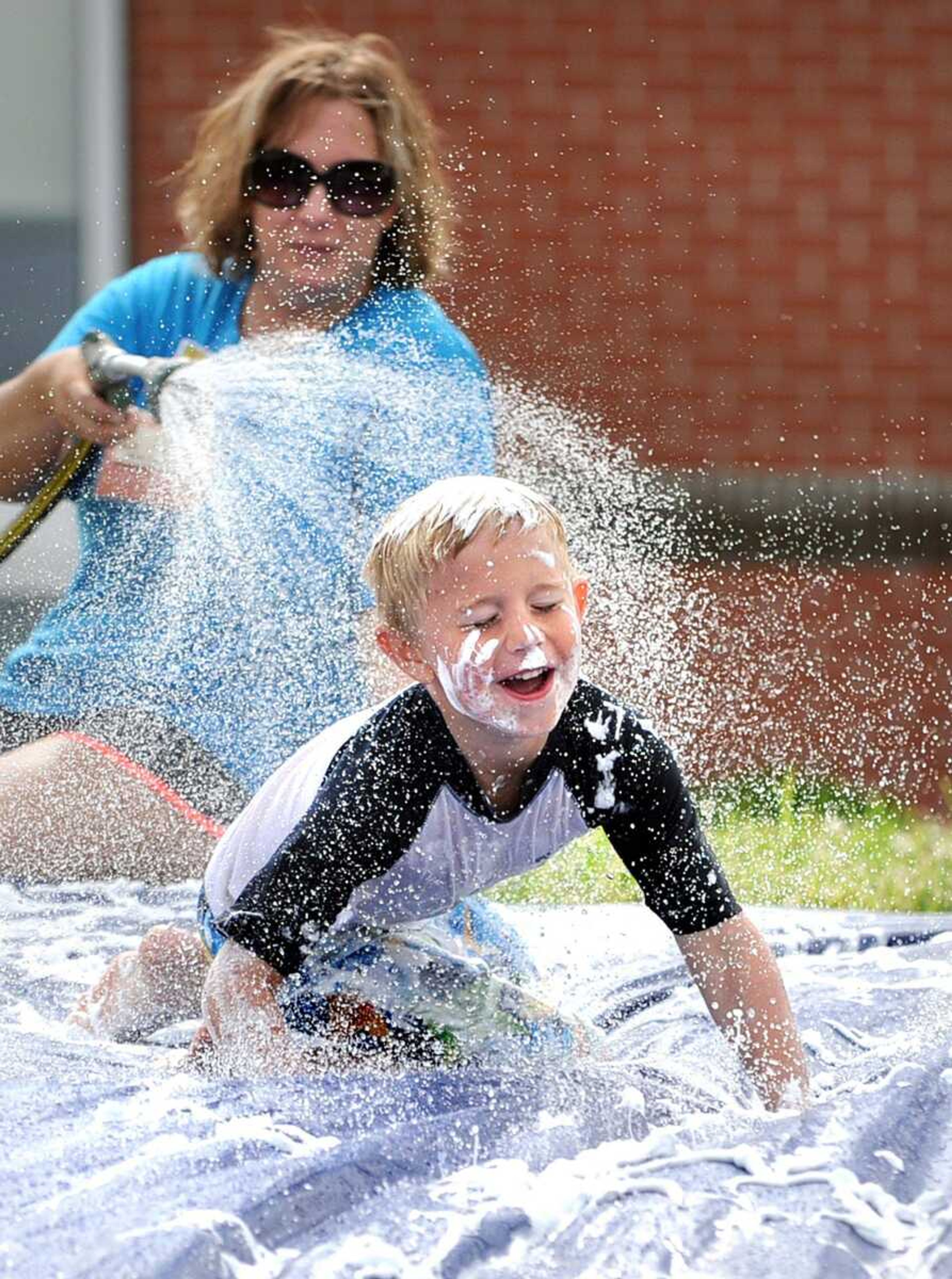 Ryan Boswell slides down a tarp covered in shaving cream as instructor Millie Aufdenberg sprays a hose behind him May 31 during the Space Odyssey summer camp at HealthPoint Fitness in Cape Girardeau. (Laura Simon)