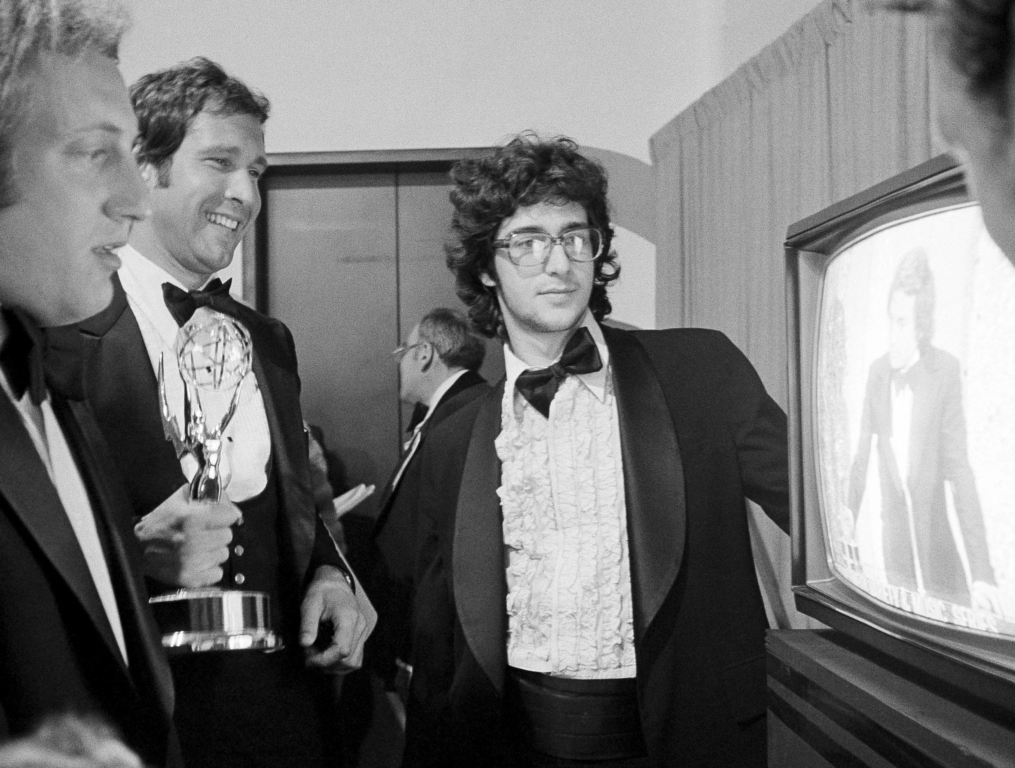 FILE - Chevy Chase, a cast member on "Saturday Night Live," holds his Emmy Award as he watches a monitor showing producer Lorne Michaels accepting another Emmy for the show, while writers Alan Zweibel, left, and Tom Davis, right, look on, during the 28th Primetime Emmy Awards in Los Angeles on May 17, 1976. (AP Photo/Reed Saxon, File)