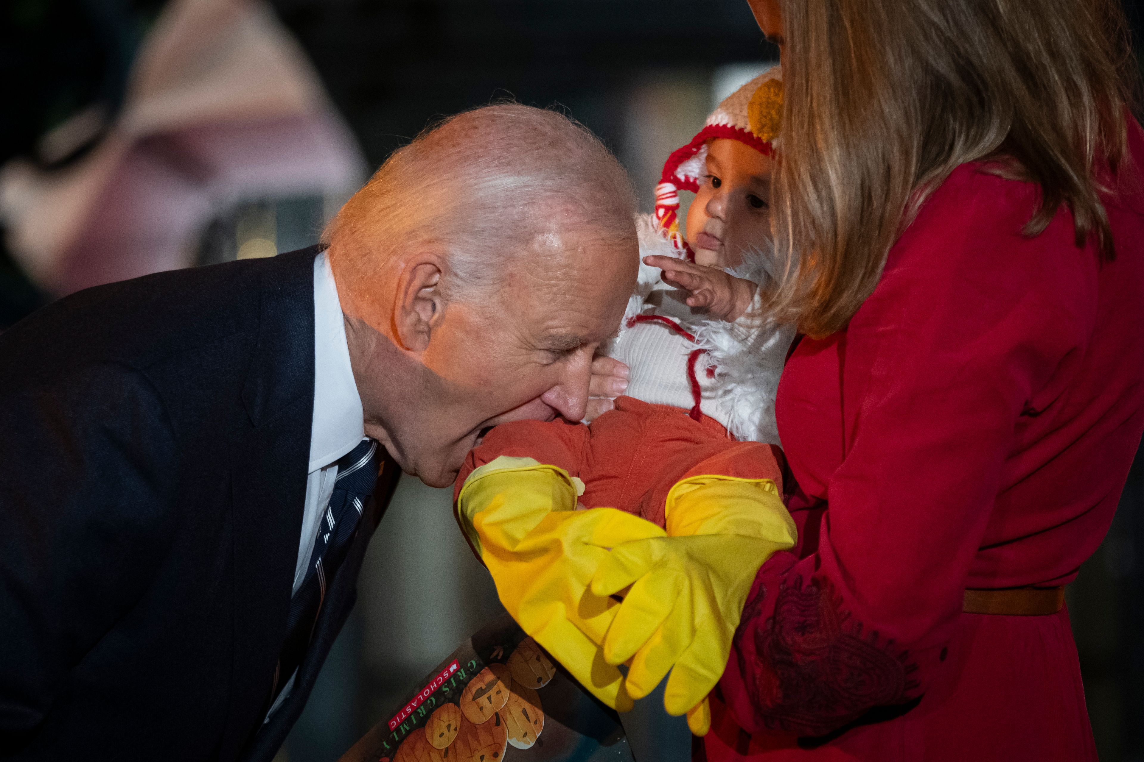 President Joe Biden jokingly bites the leg of a baby, as he and first lady Jill Biden host local area students, military-connected children, and neighborhood families for trick-or-treating, ahead of Halloween on Thursday, at the South Lawn of the White House in Washington Wednesday, Oct. 30, 2024. (AP Photo/Ben Curtis)