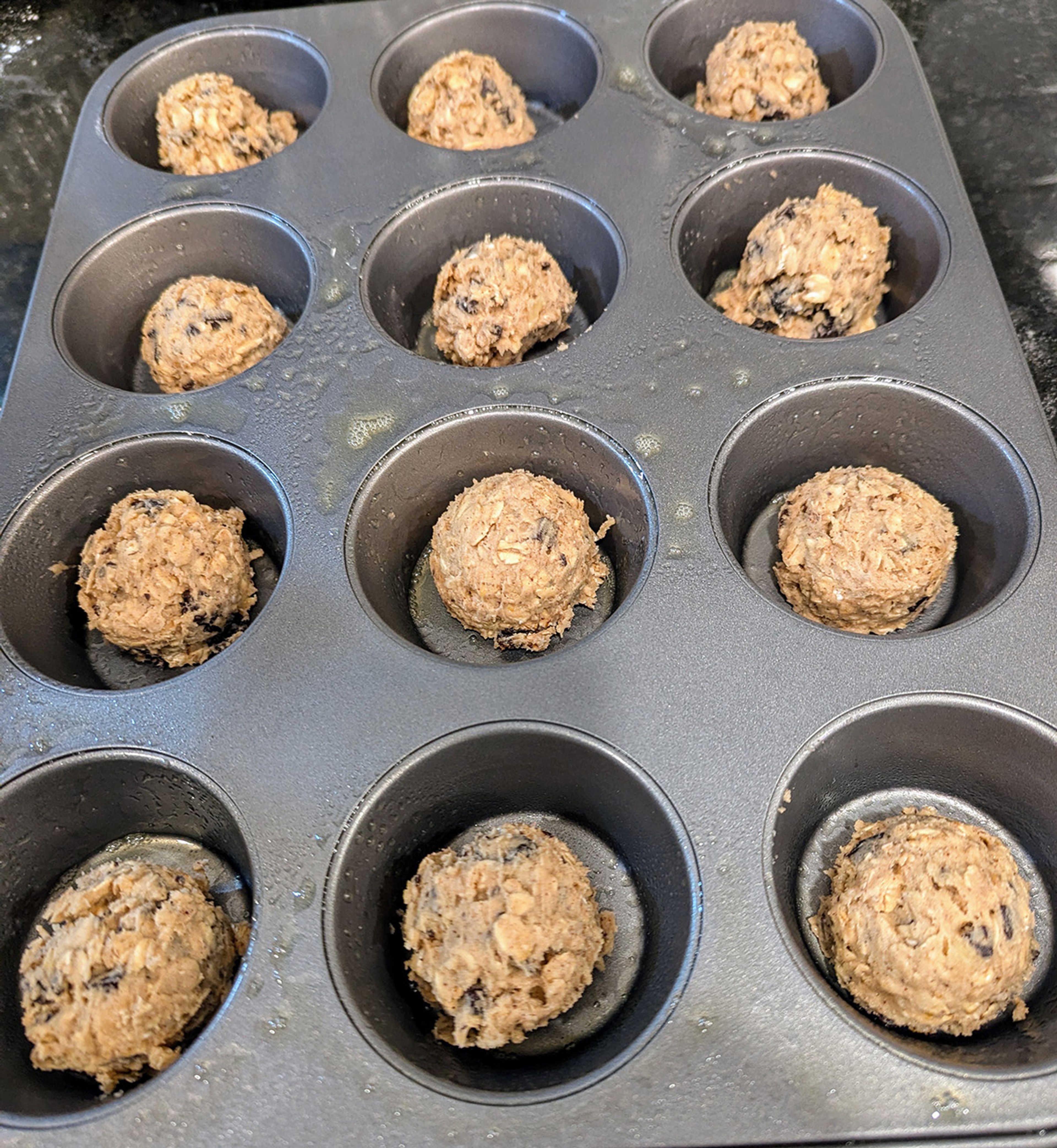 Scoops of cookie dough arranged in a muffin tin are ready for baking, a technique that will enhance their appearance and flavor.