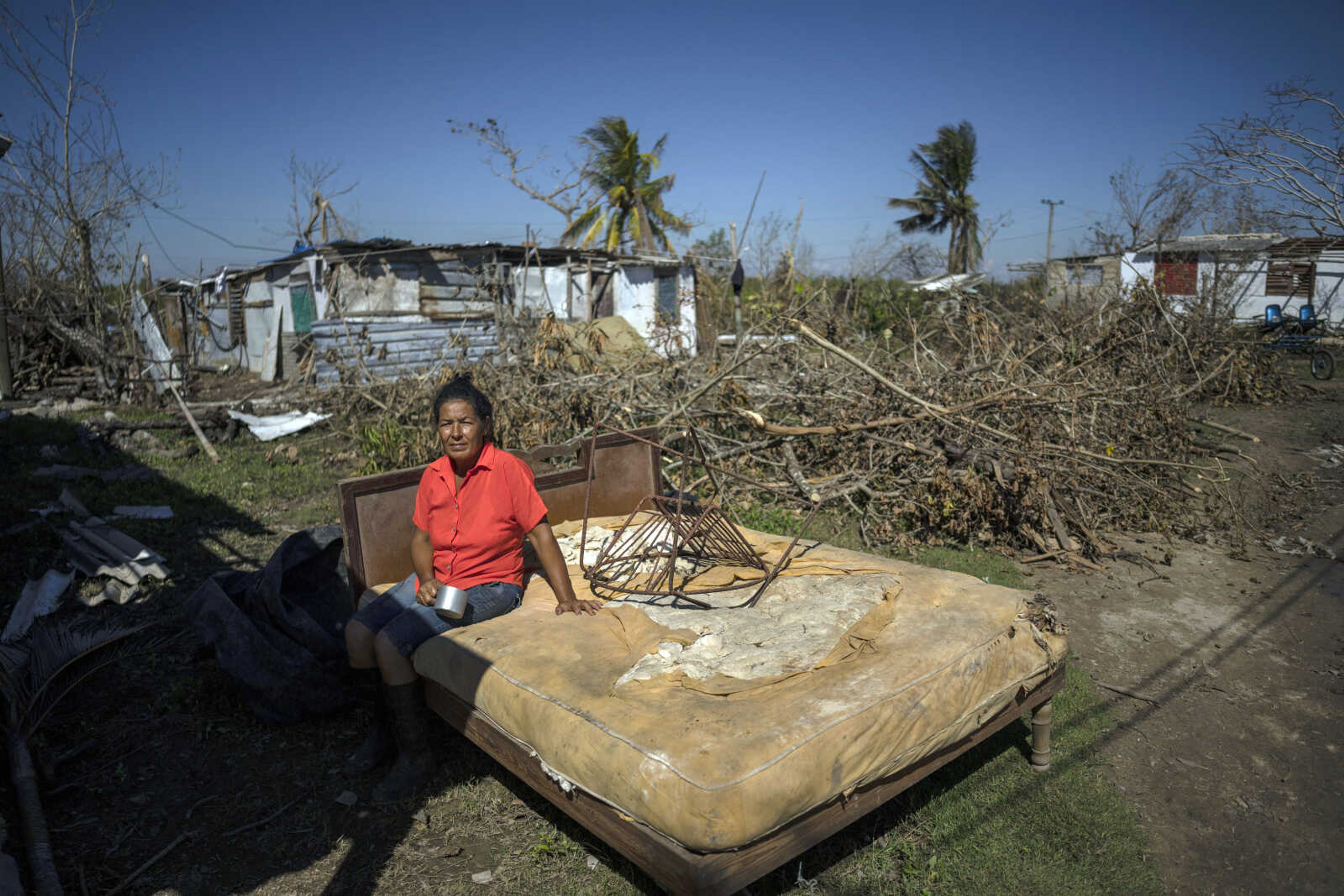 Mari Carmen Zambrano poses for a photo on her broken and wet bed Oct. 5 as she dries it outside her home that lost its roof to Hurricane Ian in La Coloma, in the province of Pinar del Rio, Cuba.