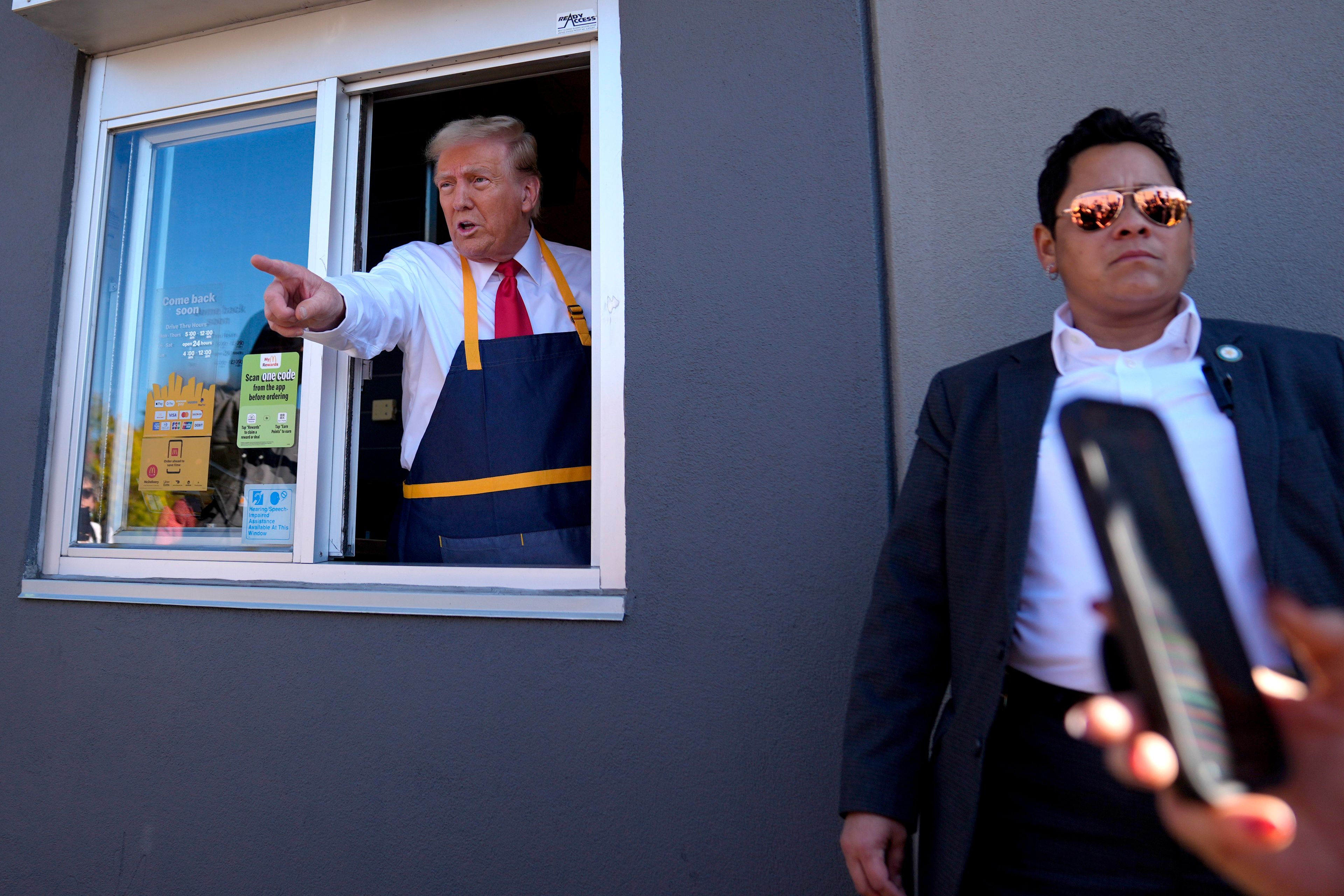 Republican presidential nominee former President Donald Trump points from a drive-thru window as a member of the Secret Service looks on during a campaign stop at a McDonald's, Sunday, Oct. 20, 2024, in Feasterville-Trevose, Pa. (AP Photo/Evan Vucci)