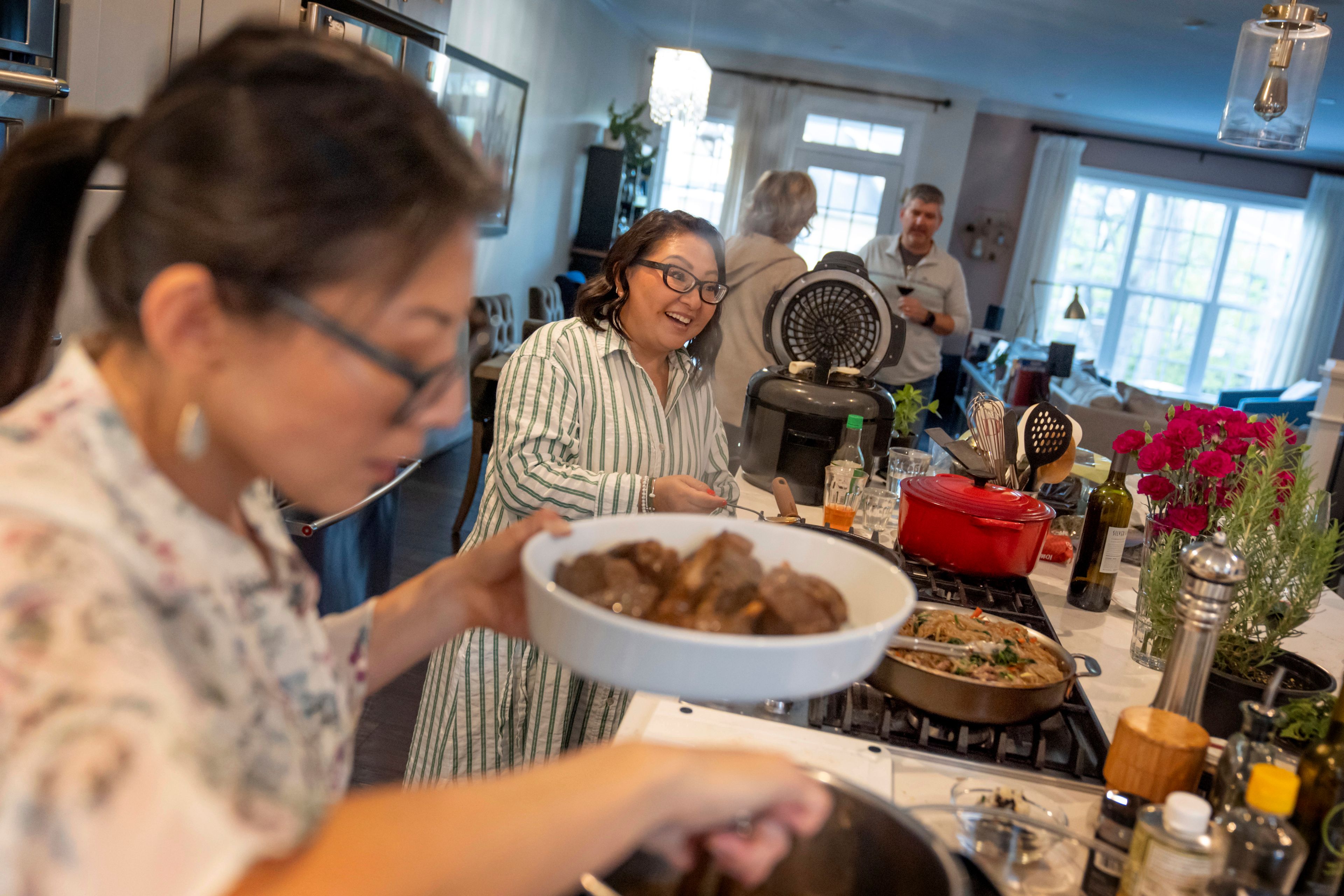 Dee Iraca, left, and her twin sister, Becca Webster, who both were adopted out of South Korea to a family in the United States, host guests at a dinner party Saturday, April 6, 2024, at Iraca's home in Davidson, N.C. Webster, a nanny with a son in college, is whimsical, chatty and easygoing. Iraca, who works as a chef and dietitian, is meticulous, serious and always on the go. (AP Photo/David Goldman)