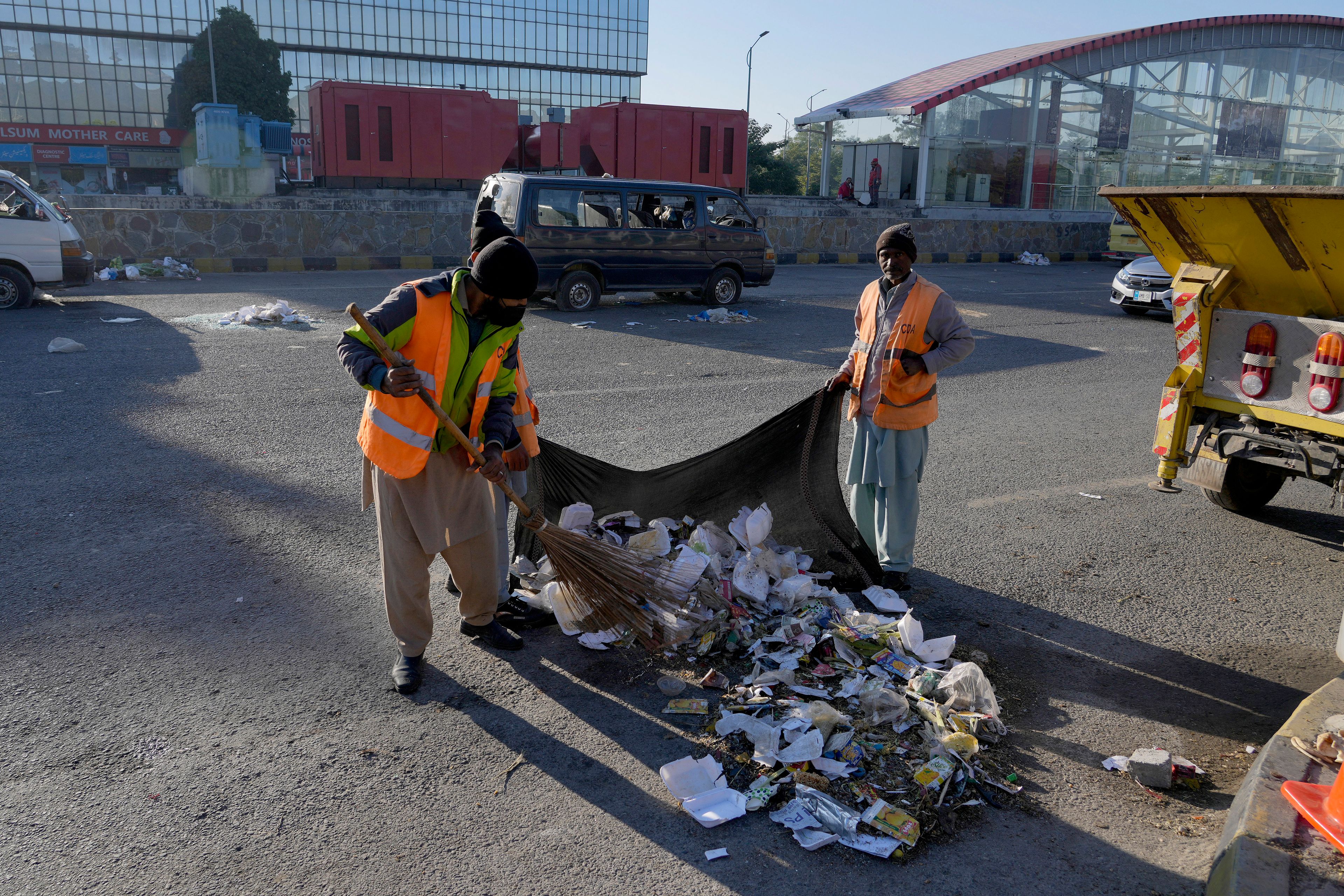 Workers clean an area near the damaged vehicles left behind by supporters of imprisoned former Prime Minister Imran Khan's Pakistan Tehreek-e-Insaf party when security forces launched an operation Tuesday night to disperse them, in Islamabad, Pakistan, Wednesday, Nov. 27, 2024. (AP Photo/Anjum Naveed)