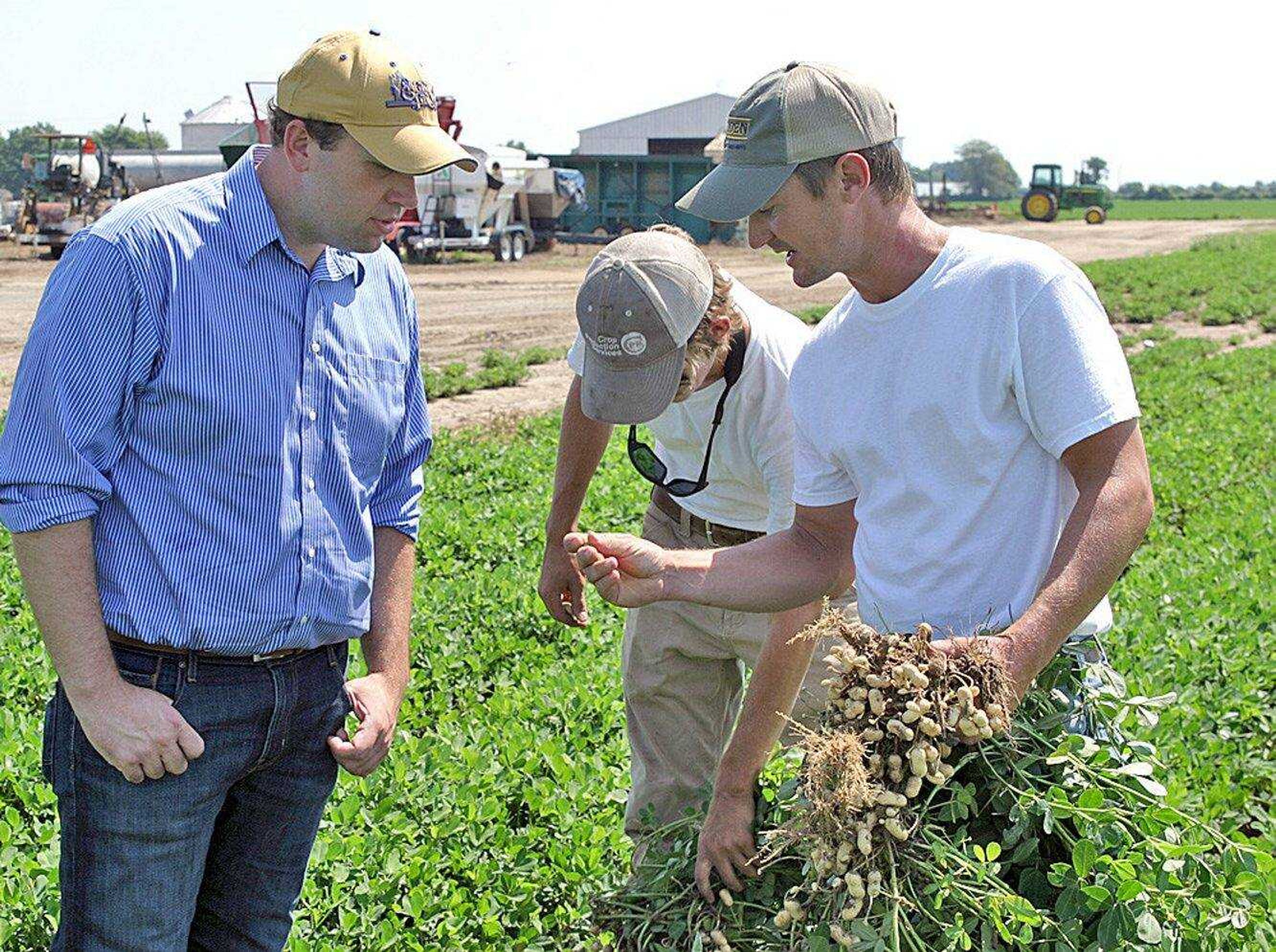 U.S. Rep. Jason Smith, left, looks as Hunter Deane, center, and Matt Deane shake off dirt from the roots of a peanut plant in the fields of the Triple D Farms in Sikeston, Missouri.