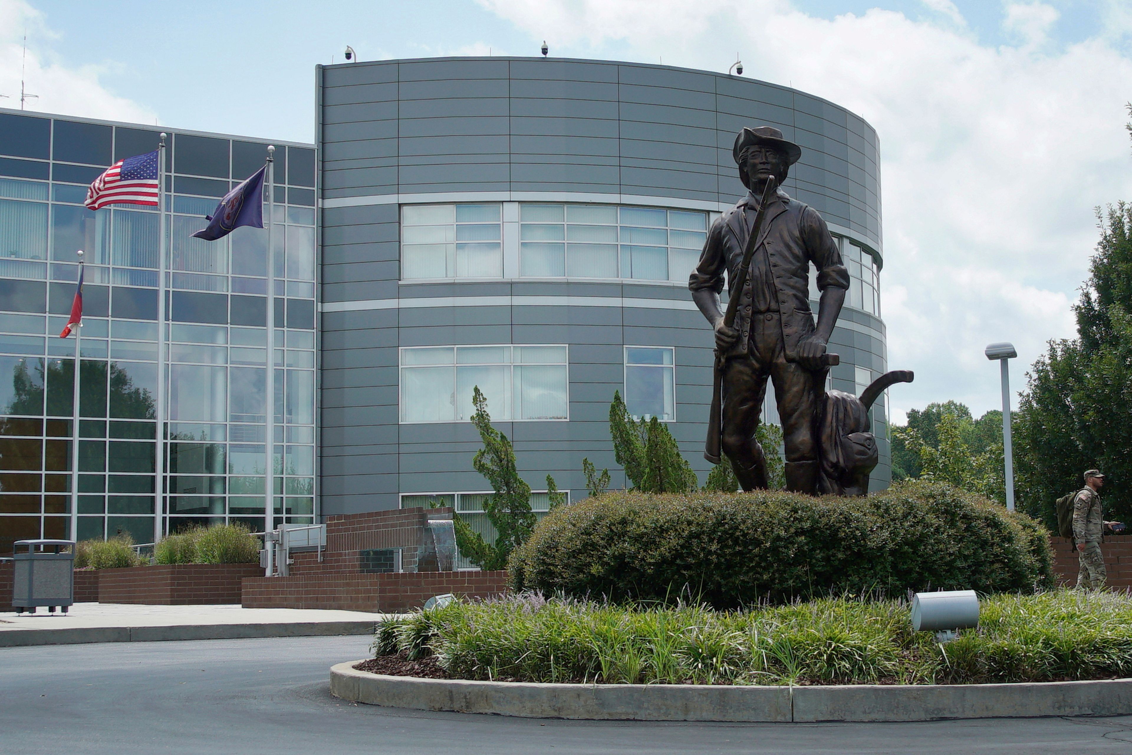 A soldier in camouflage, right, walks past the "Minute Man" statue outside the National Guard headquarters in Raleigh, N.C., on Tuesday, July 30, 2024. (AP Photo/Allen G. Breed)