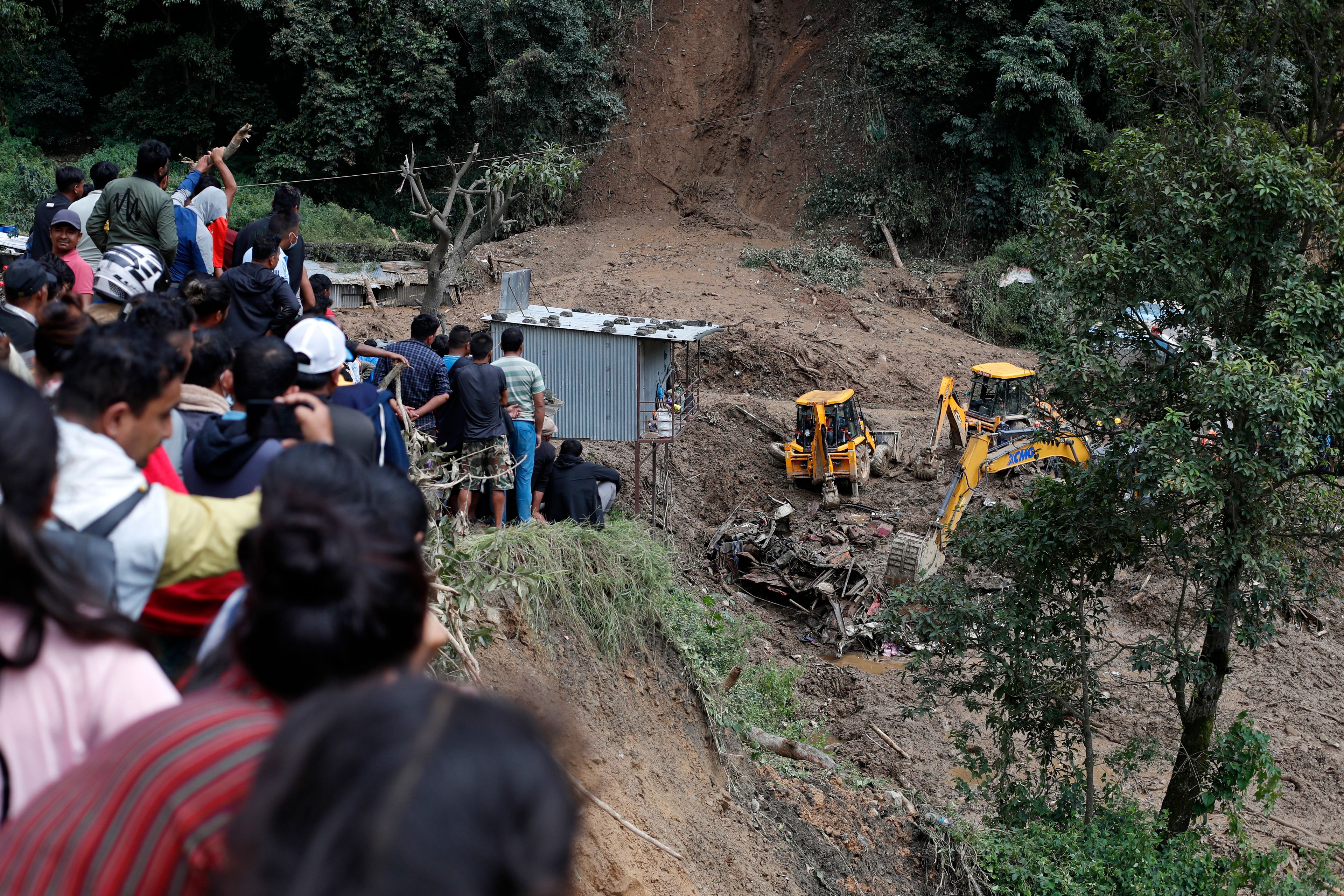 People watch earthmovers removing automobile debris and the dead bodies of victims trapped under a landslide caused by heavy rains in Kathmandu, Nepal, Sunday, Sept. 29, 2024. (AP Photo/Sujan Gurung)