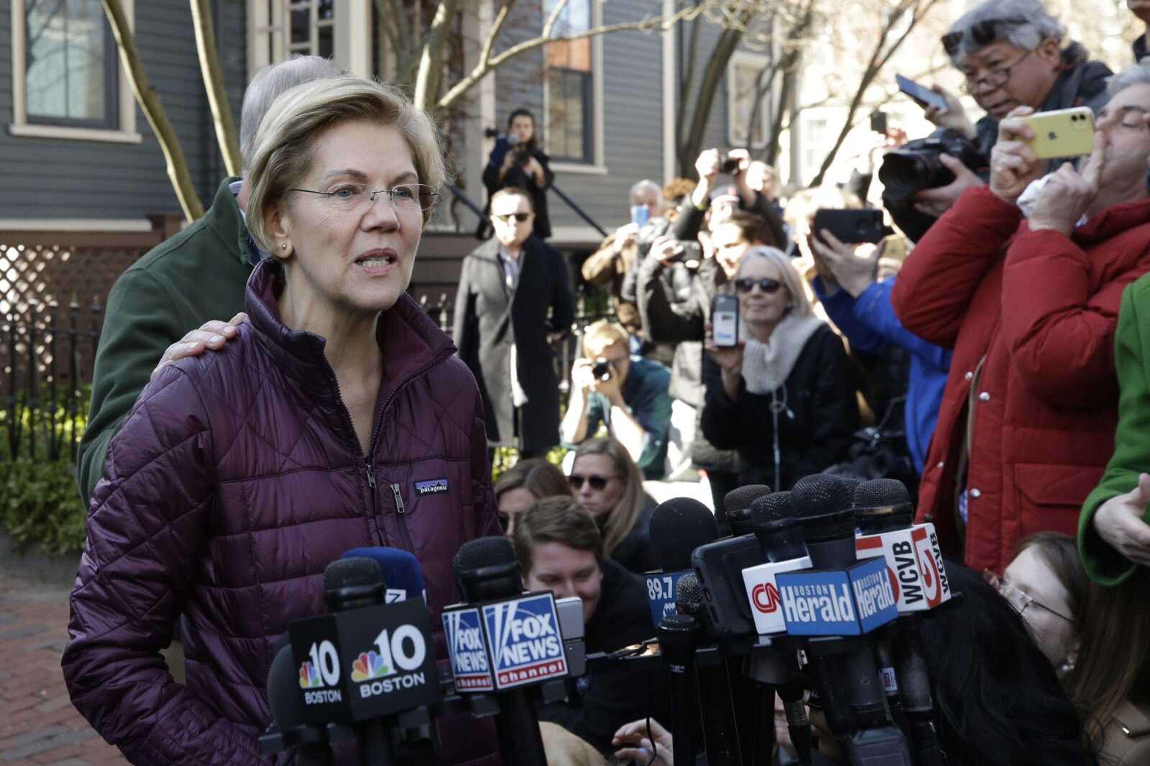 Sen. Elizabeth Warren, D-Mass., with her husband Bruce Mann's hand on her shoulder, speaks to the media outside her home Thursday in Cambridge, Massachusetts, after she dropped out of the Democratic presidential race.