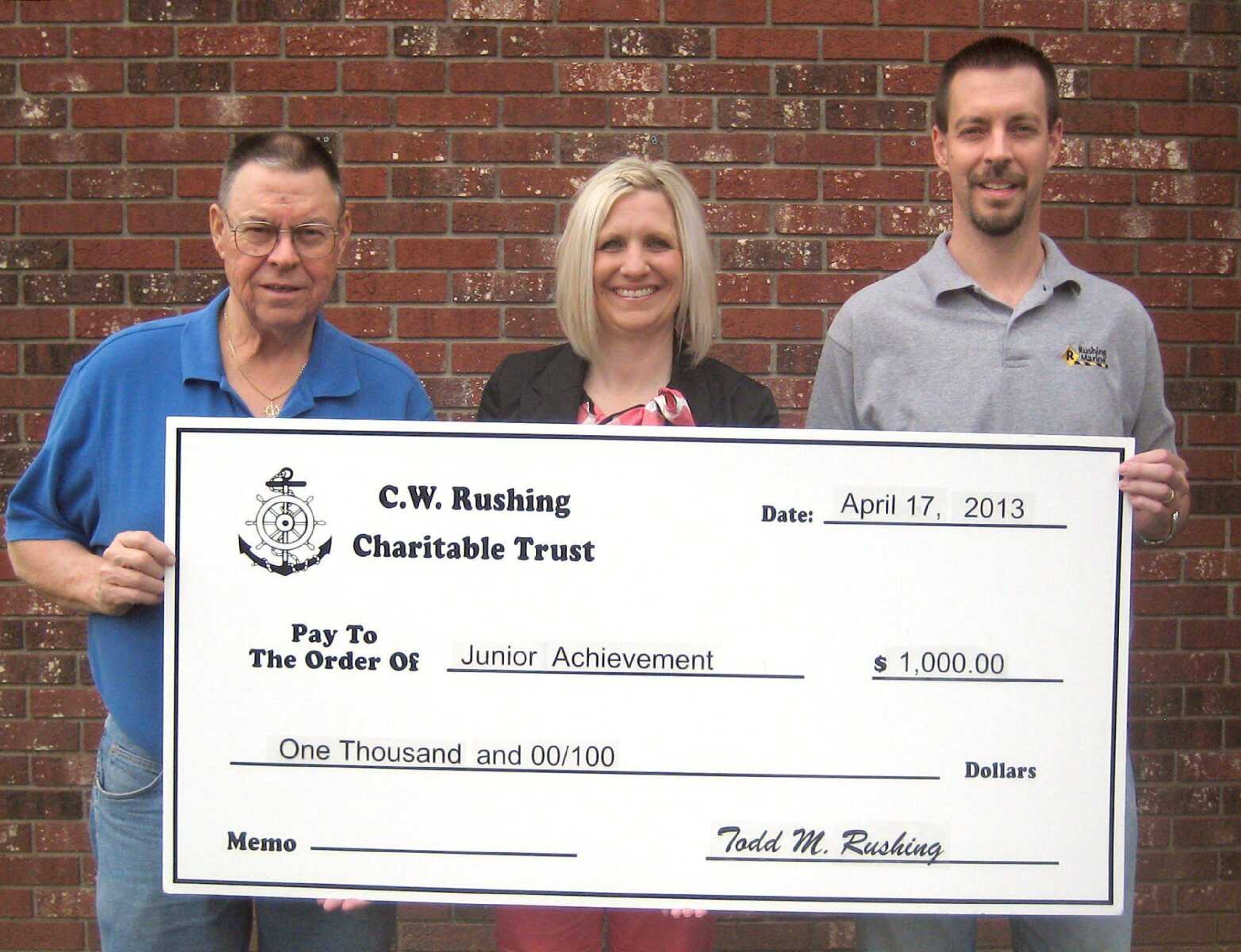 Michael Rushing, left, and Todd Rushing, representing the C.W. Rushing Charitable Trust, present at $1,000 donation to Becki Arends, representing Junior Achievement. The funds came from proceeds of the 14th annual Captain Woody Rushing Golf Tournament that was held at Kimbeland Country Club in Jackson.