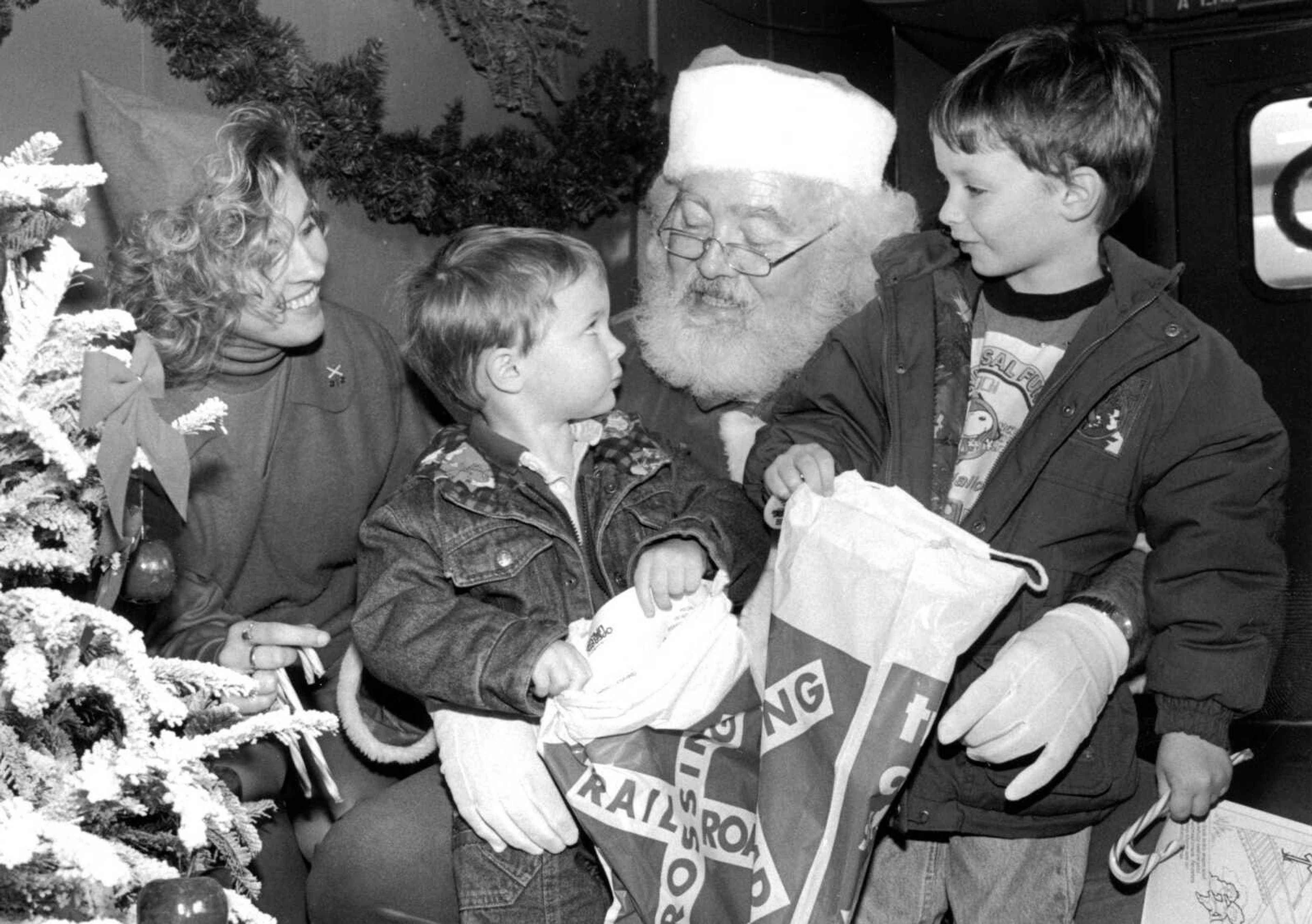 Published Dec. 17, 1992.
Aboard the caboose of the Southern Pacific Santa Special, Santa Claus, portrayed by J.R. Johnson, and his elf, daughter Tracy Johnson, spread some Christmas cheer in Scott City Wednesday to Eric Lutes, left, and his brother, Ryan Lutes. The train is making stops in six states so Santa can visit with children and granchildren of railroad employees. (Southeast Missourian archive)