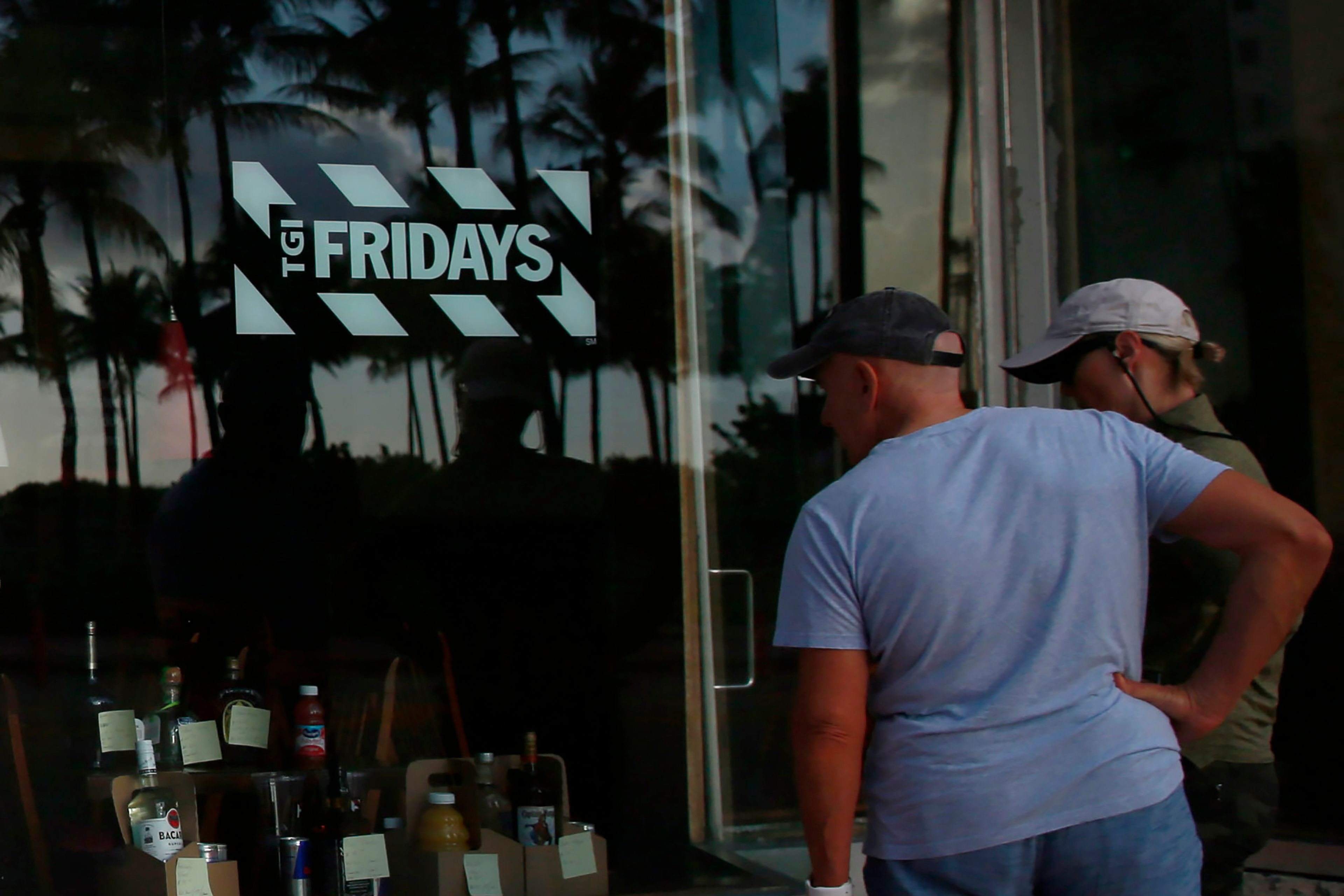 FILE - People peek into a window of a TGI Friday's restaurant to see what they are serving to-go on Wednesday, March 25, 2020, in Miami Beach, Fla. (AP Photo/Brynn Anderson, File)