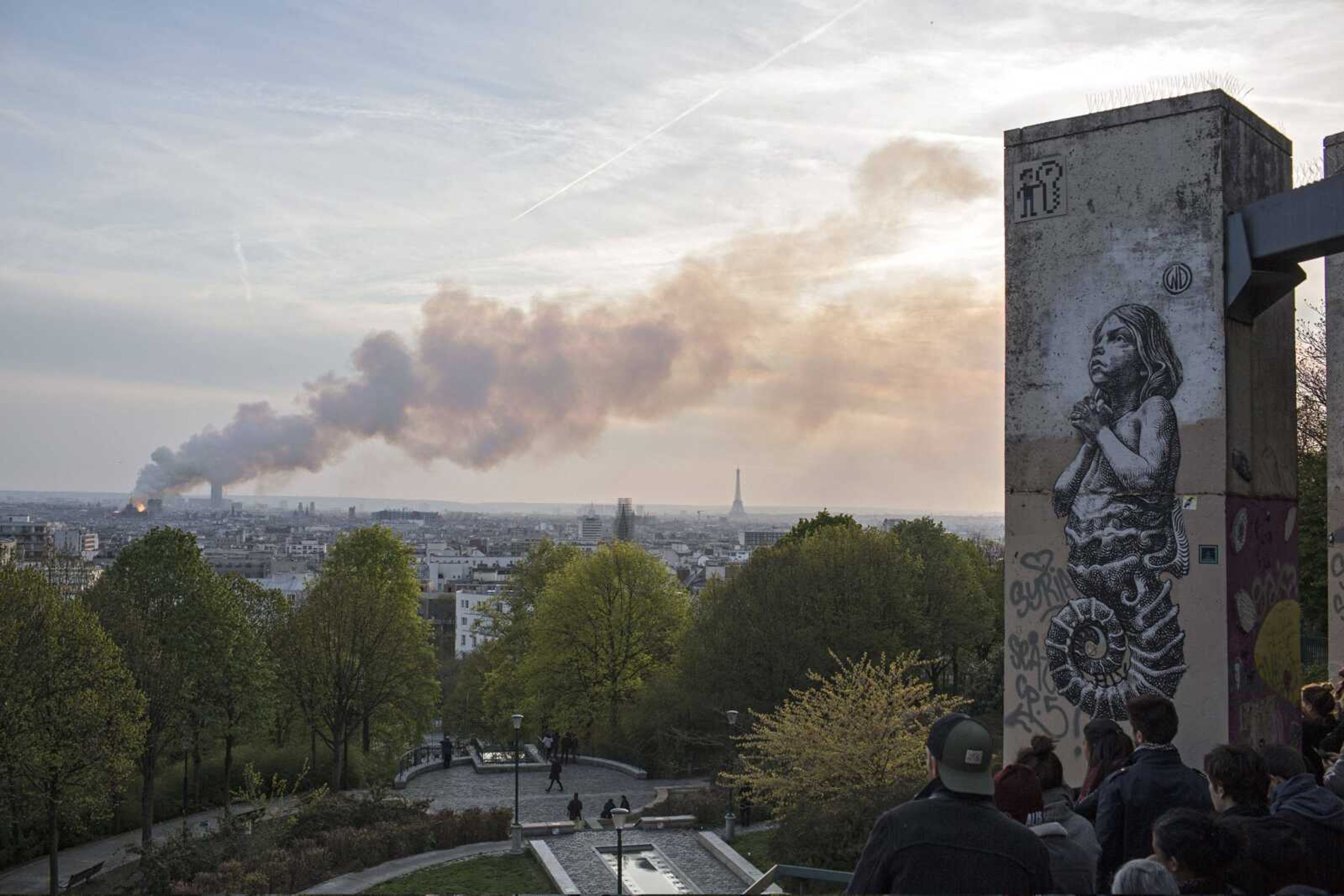 People watch Notre Dame cathedral burning in Paris, Monday, April 15, 2019. Massive plumes of yellow brown smoke is filling the air above Notre Dame Cathedral and ash is falling on tourists and others around the island that marks the center of Paris. (AP Photo/Rafael Yaghobzadeh)