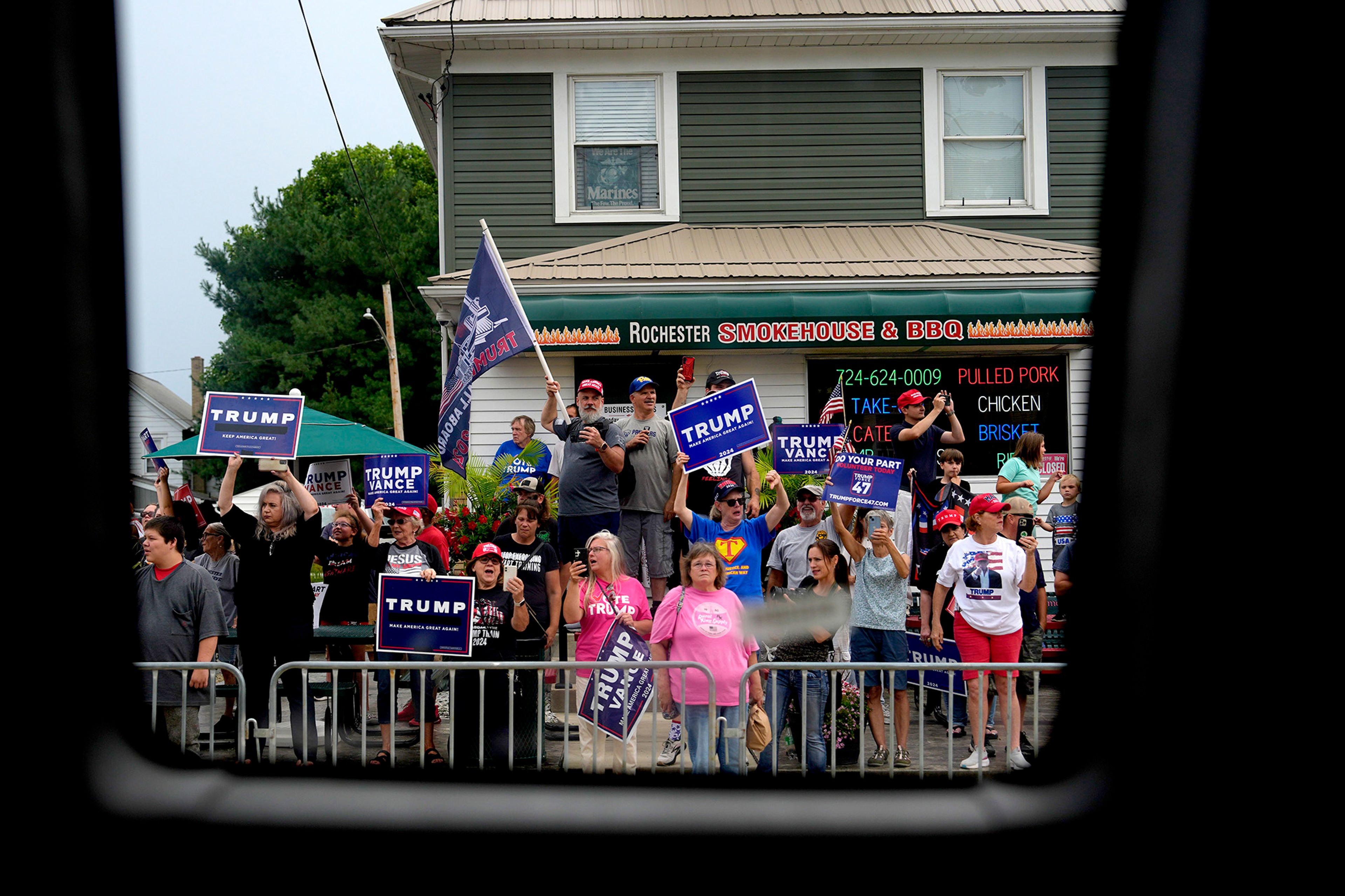 Supporters of Republican presidential candidate former President Donald Trump look on as a bus carrying Democratic presidential nominee Vice President Kamala Harris passes by following a campaign event, Sunday, Aug. 18, 2024, in Rochester, Pa.