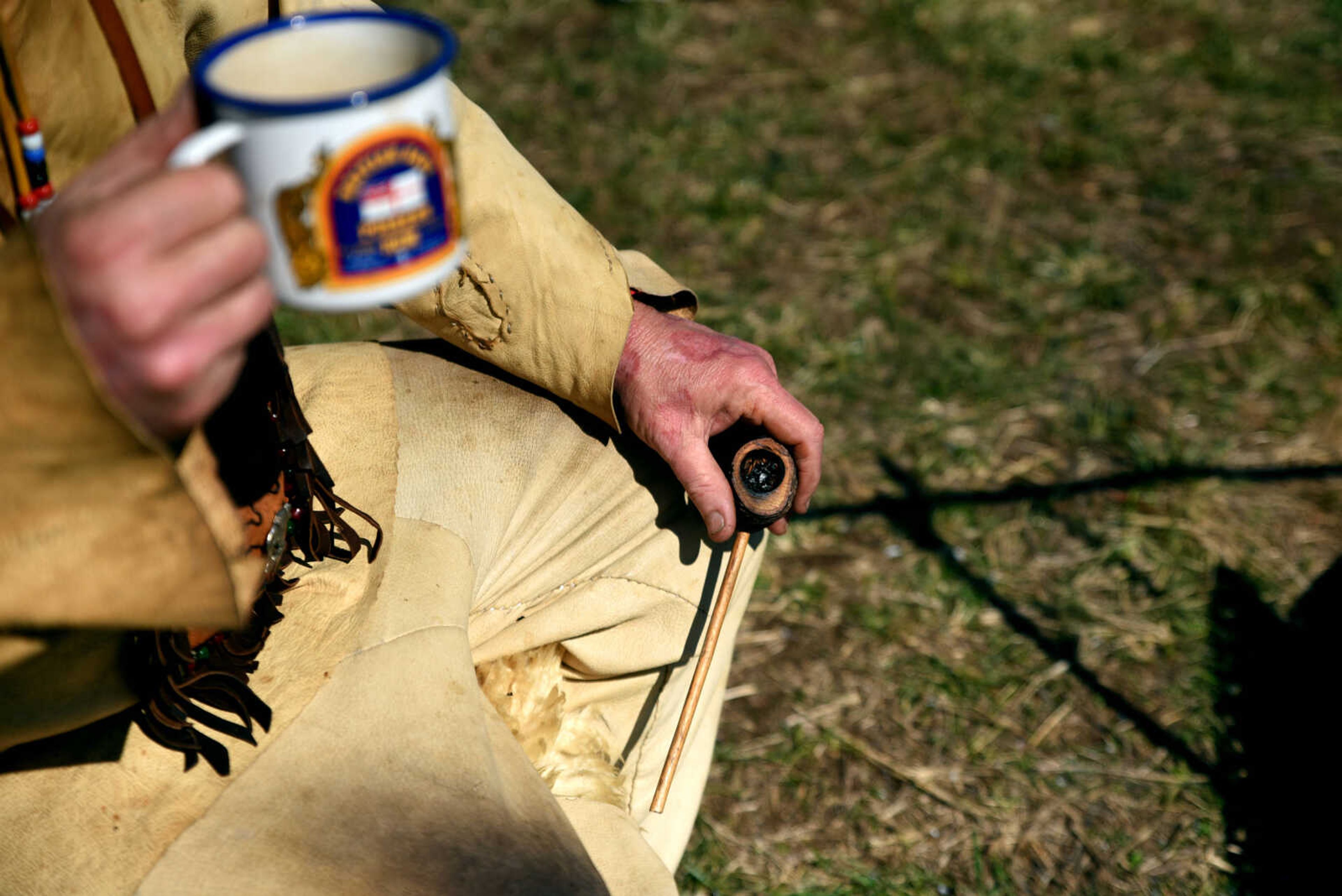 Bud Lewey of the "Ded Squirrels" holds a coffee mug and a pipe while sitting in the sun at his encampment during the second annual Eastern Ozark Rendezvous held at Bark's Planation Saturday, March 17, 2018, in Glenallen.