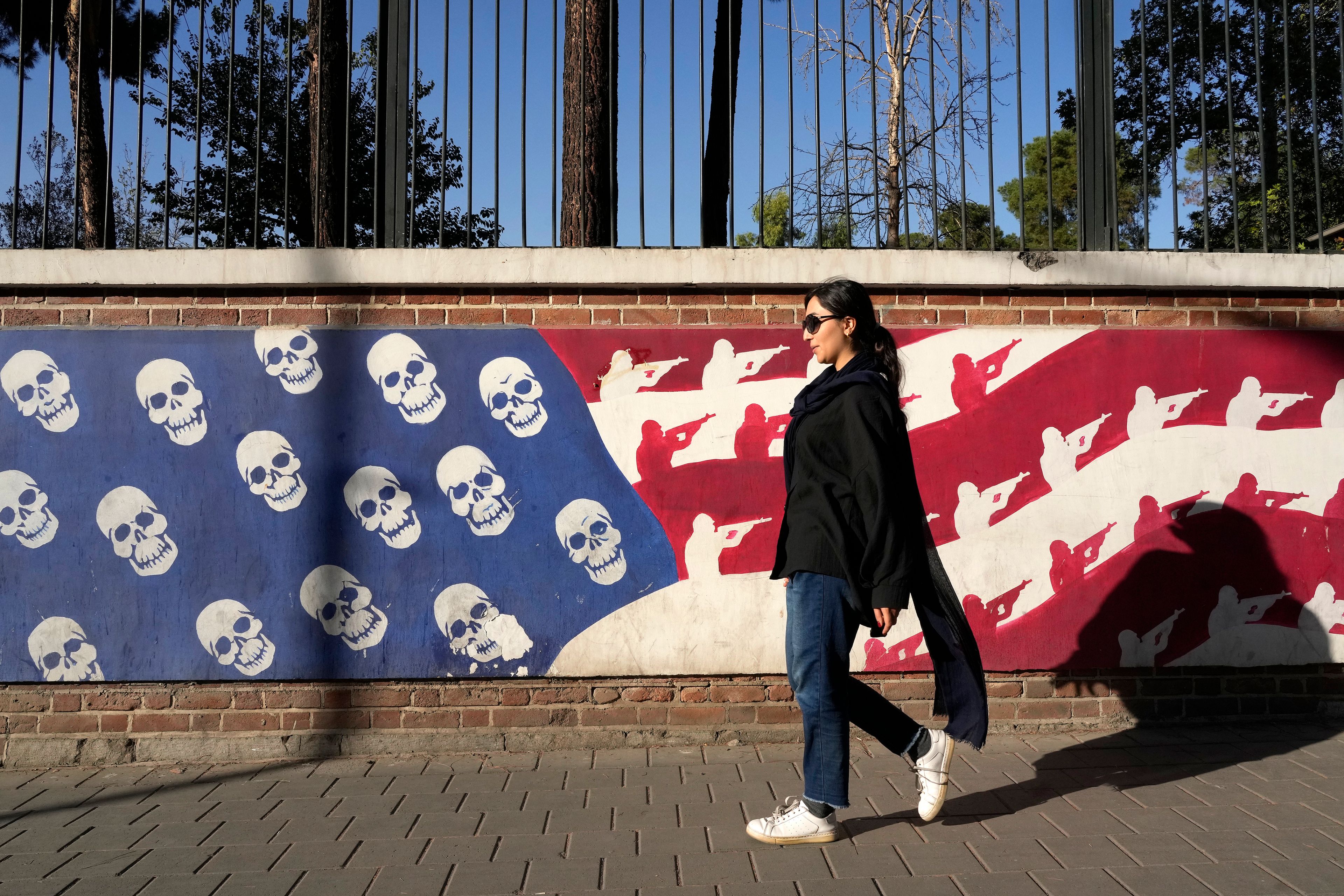 An Iranian woman walks past a satirised image of the U.S. flag on the wall of former U.S. embassy, in Tehran, Iran, Tuesday, Oct. 22, 2024. (AP Photo/Vahid Salemi)