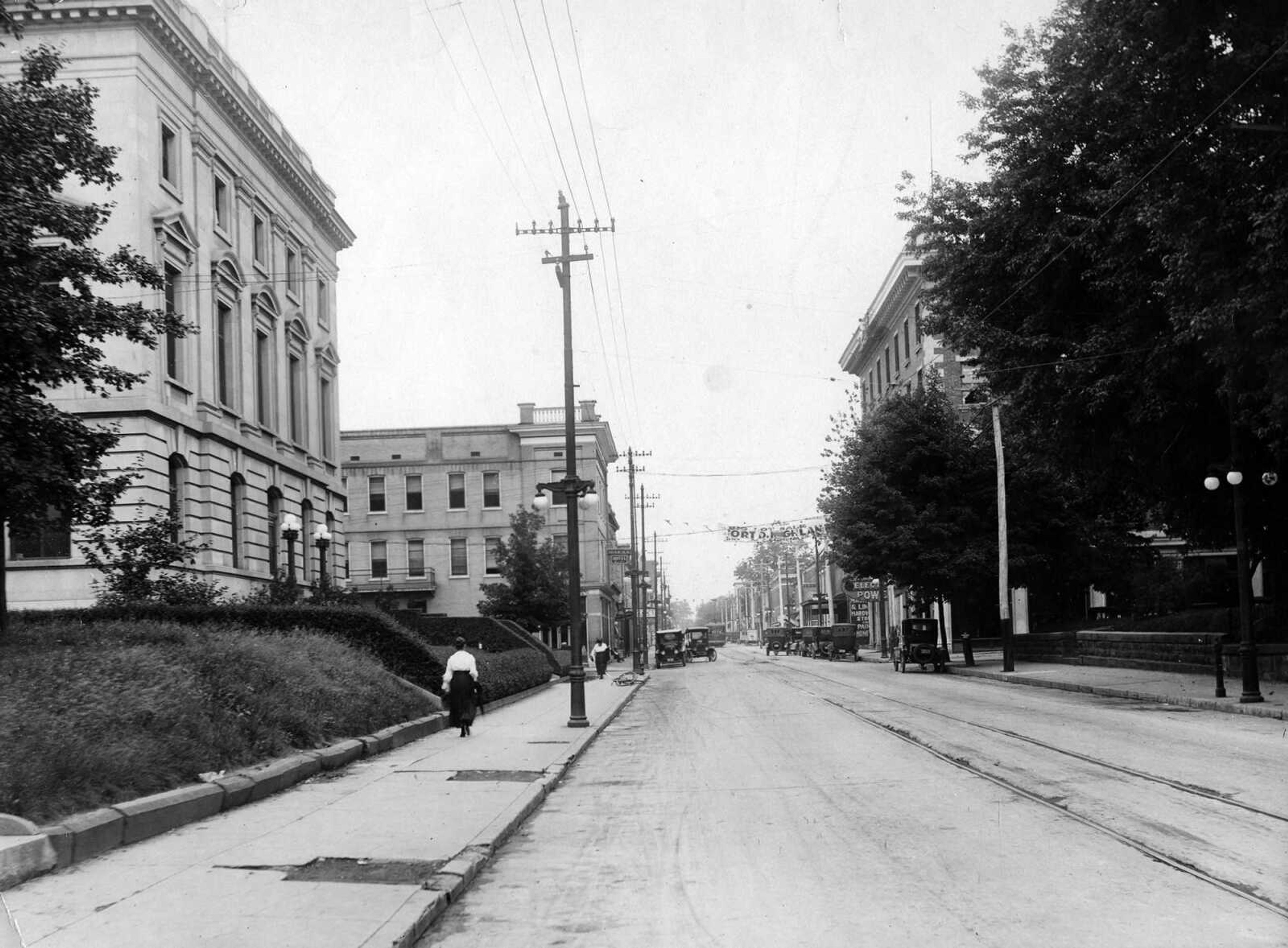 A banner advertising the sale of lots in the "Fort D Highlands" fluttered above the 400 block of Broadway in this circa 1922 photo. At left is the Post Office/Federal Building and the Idan-Ha Hotel. At right, partially obscured by trees, is the H-H Building, with a man painting the coping of the building.