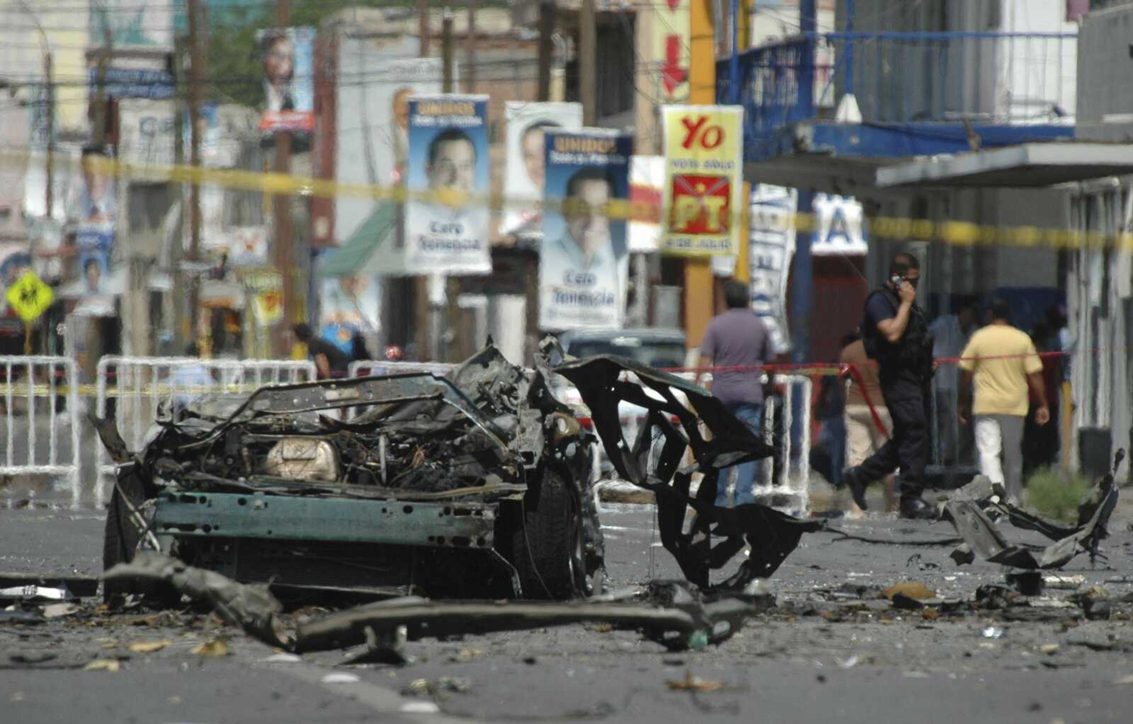 The remains of a vehicle are cordoned off Friday in a street in the northern border city of Ciudad Juarez, Mexico. Mexican investigators ran forensic tests to determine whether drug gangs used a car bomb in an attack on police patrol trucks that killed two officers and wounded nine people Thursday. (Associated Press)