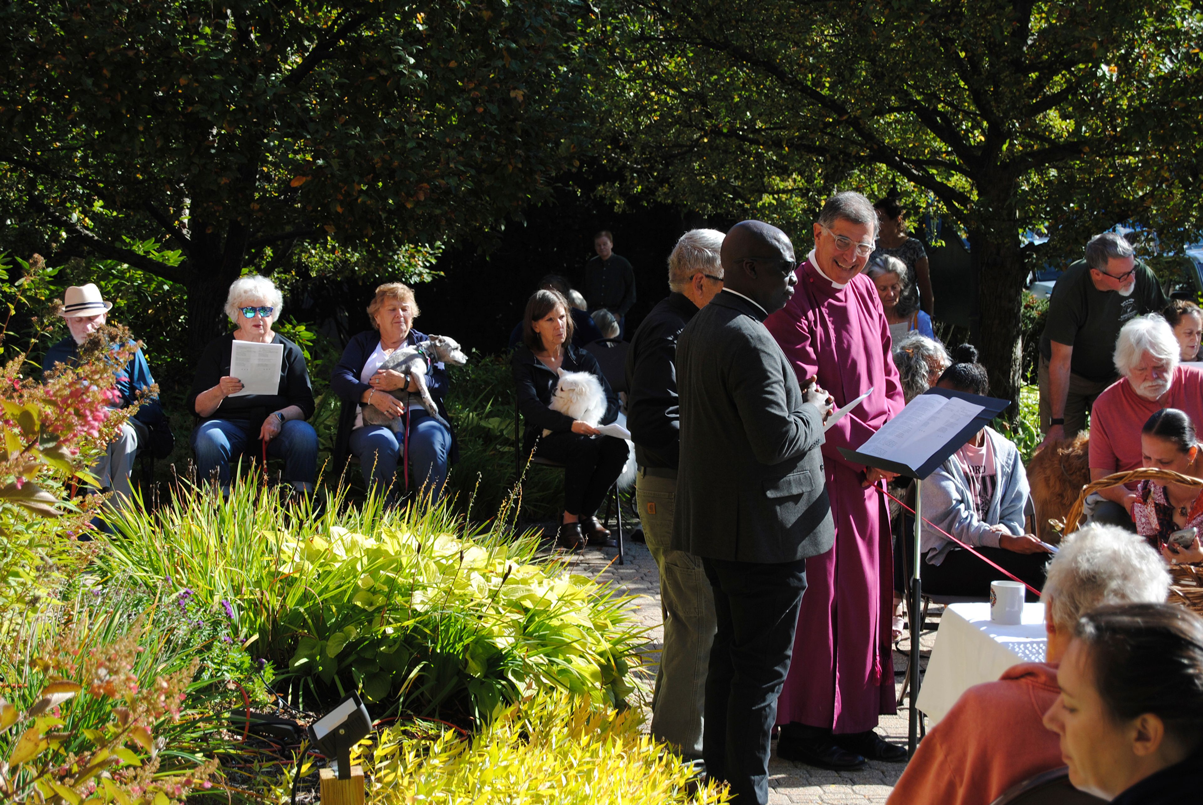 Dozens of people brought their dogs and photos of other pets to be blessed by Haitian immigrant Jean Beniste, center in black suit, on Saturday, Oct. 5, 2024, in the garden of St. Paul's Episcopal Church in Concord, N.H., where Beniste is the rector. (G. Jeffrey MacDonald via AP)